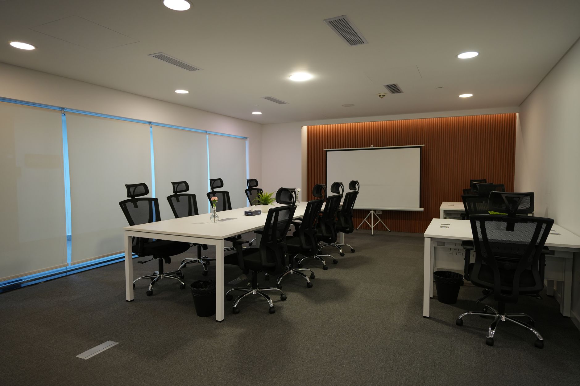 A glass-walled conference room in a venture capital office with a projector displaying a multi-line financial projection chart on a white screen, with empty leather chairs arranged around a long table
