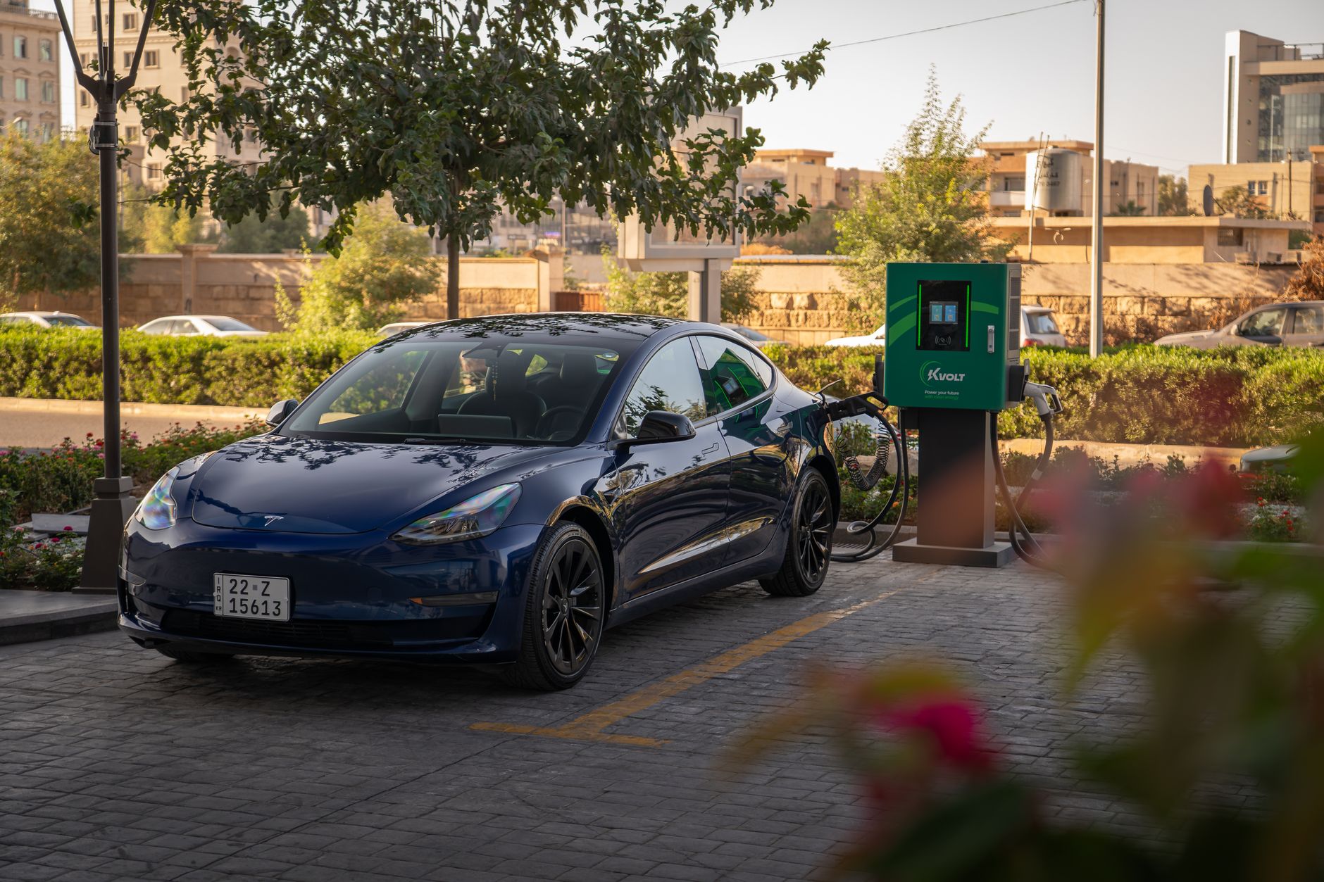 rows of electric vehicle charging stations in an empty carpark outside a modern automotive manufacturing facility