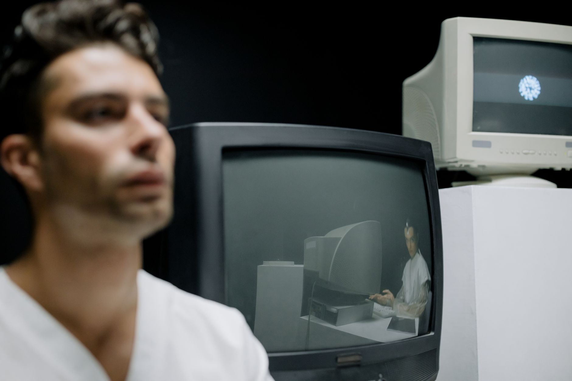 close-up of a computer monitor displaying rendered simulation frames of a robotic arm interacting with objects on a table, in a dimly lit research laboratory