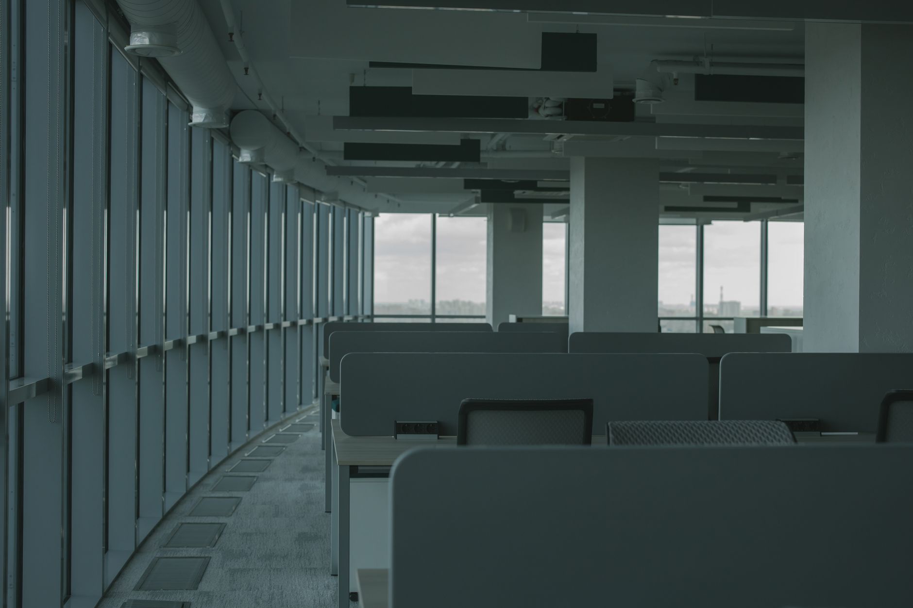 empty office corridor with rows of vacant workstations and dim overhead lighting stretching into the distance