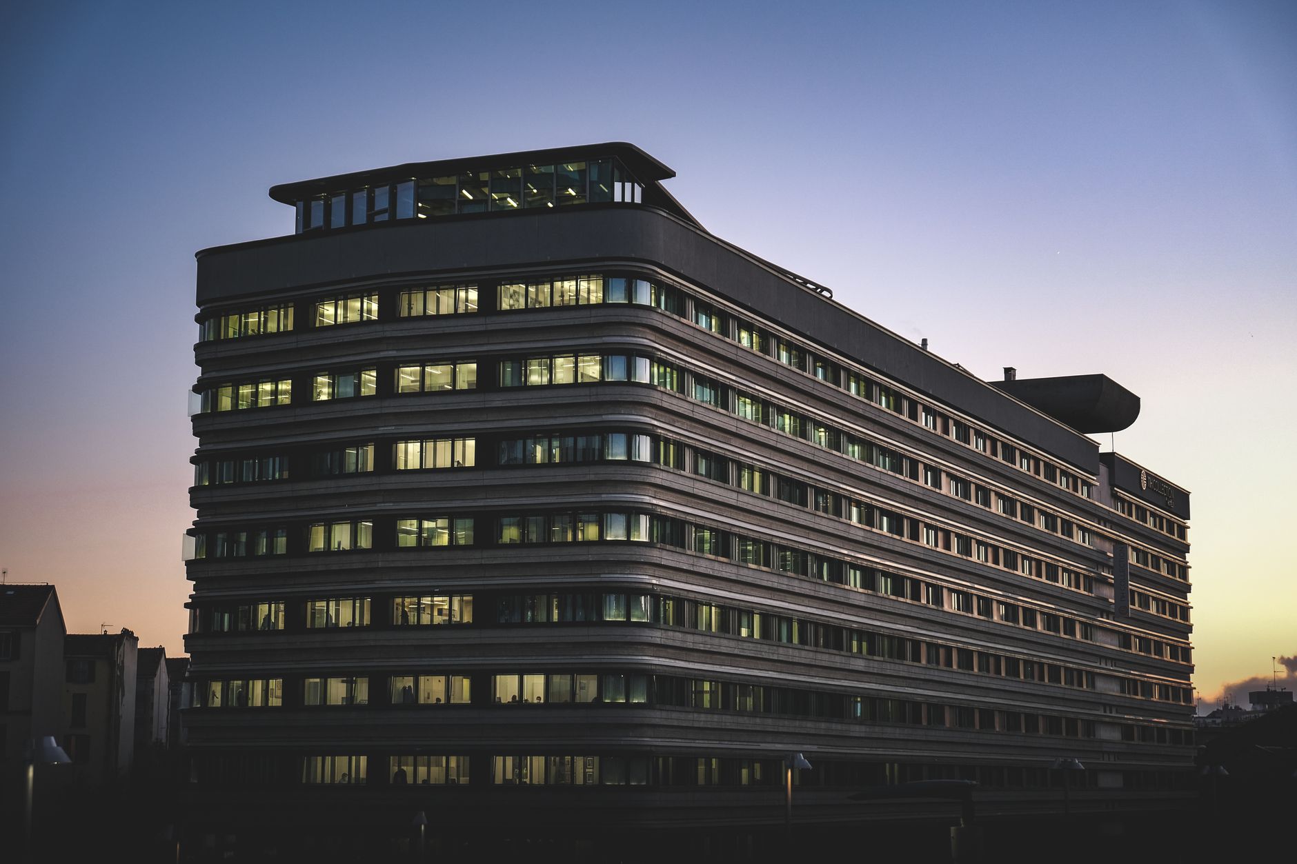 exterior of a large urban hospital building at dusk with lit windows and an ambulance bay visible in the foreground