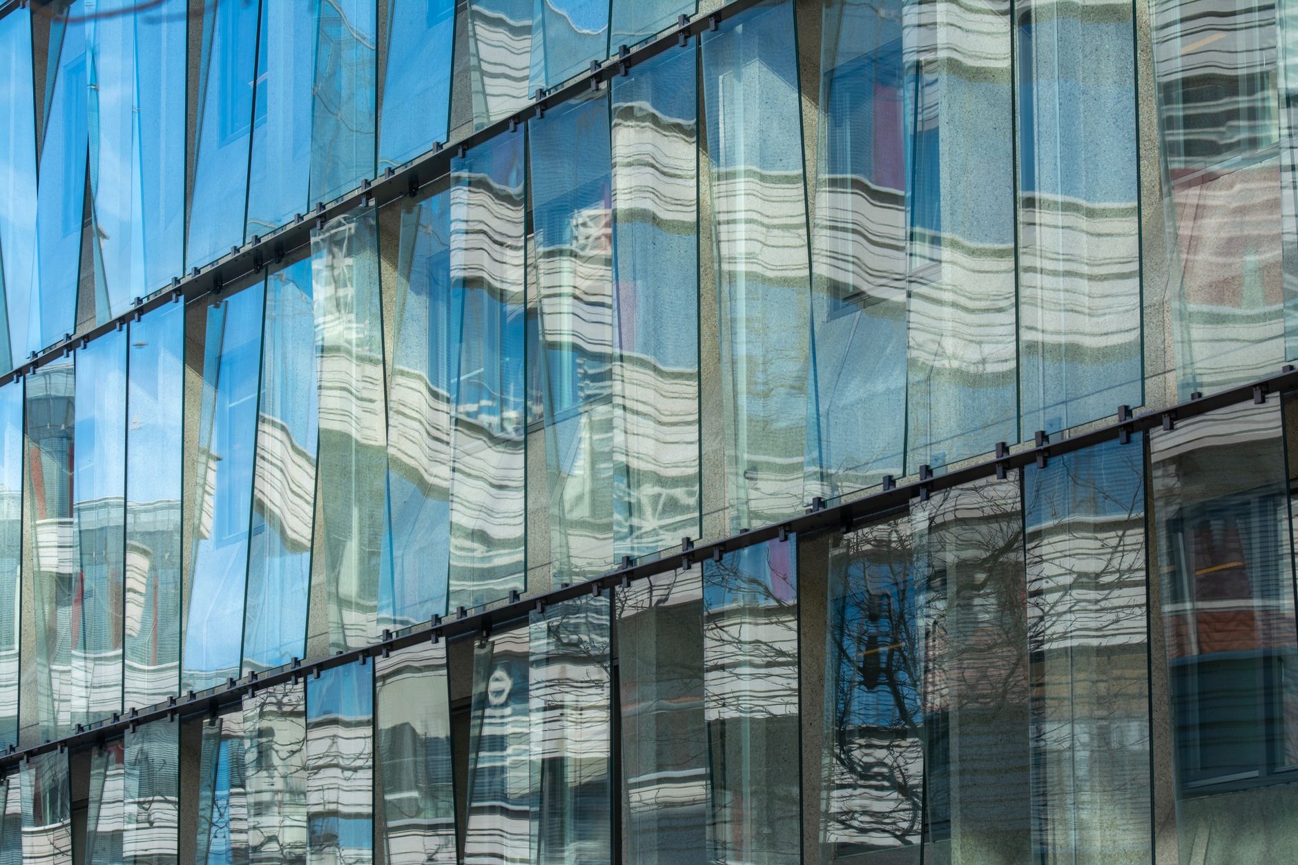 exterior of a glass-fronted technology campus building at dusk, with interior office lighting visible through floor-to-ceiling windows reflecting off a wet plaza surface