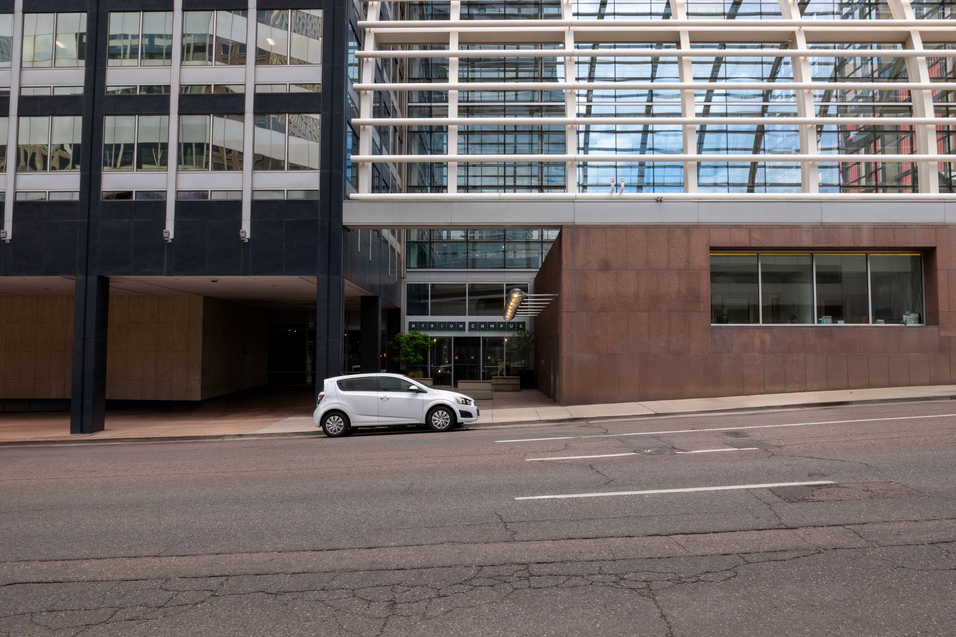 exterior of a mid-rise glass office building in a suburban American business park, with a vacancy sign visible near the entrance and an empty parking lot in the foreground