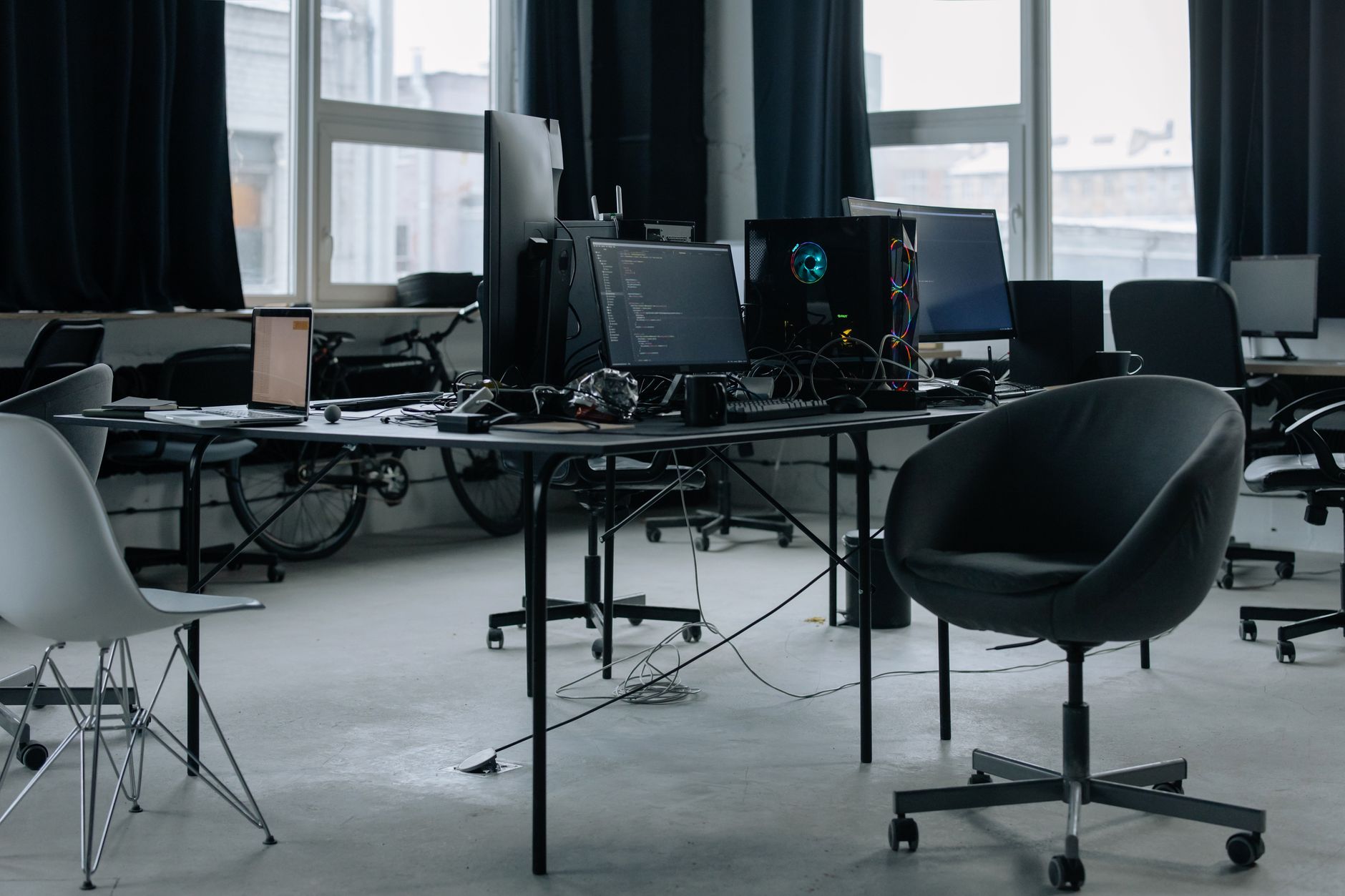 interior of a largely empty open-plan office floor with rows of unused desks, dusty monitors, and natural light filtering through floor-to-ceiling windows