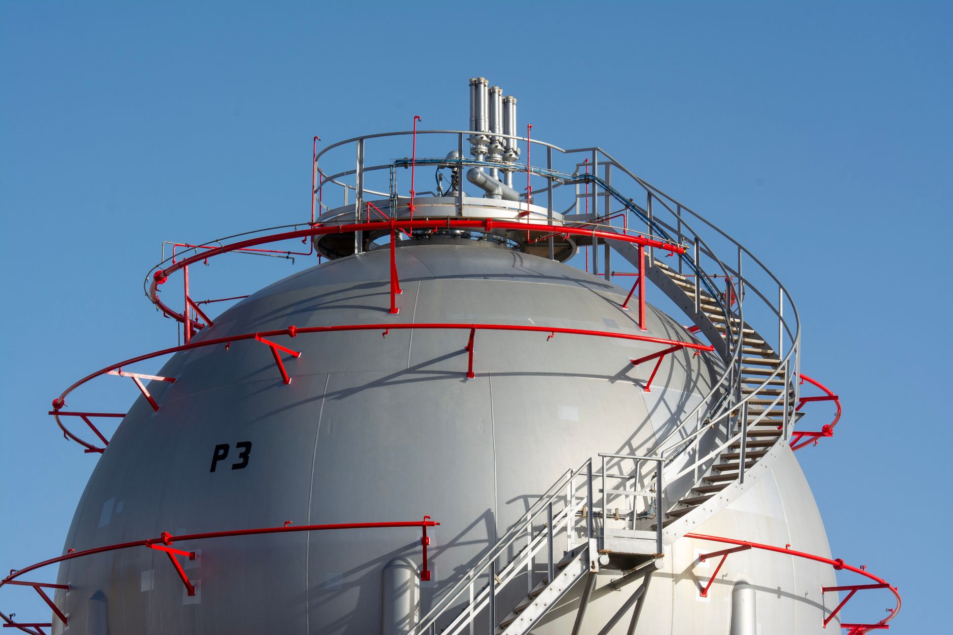 rows of crude oil storage tanks at a large onshore terminal under a hazy industrial sky, with pipeline infrastructure visible in the foreground