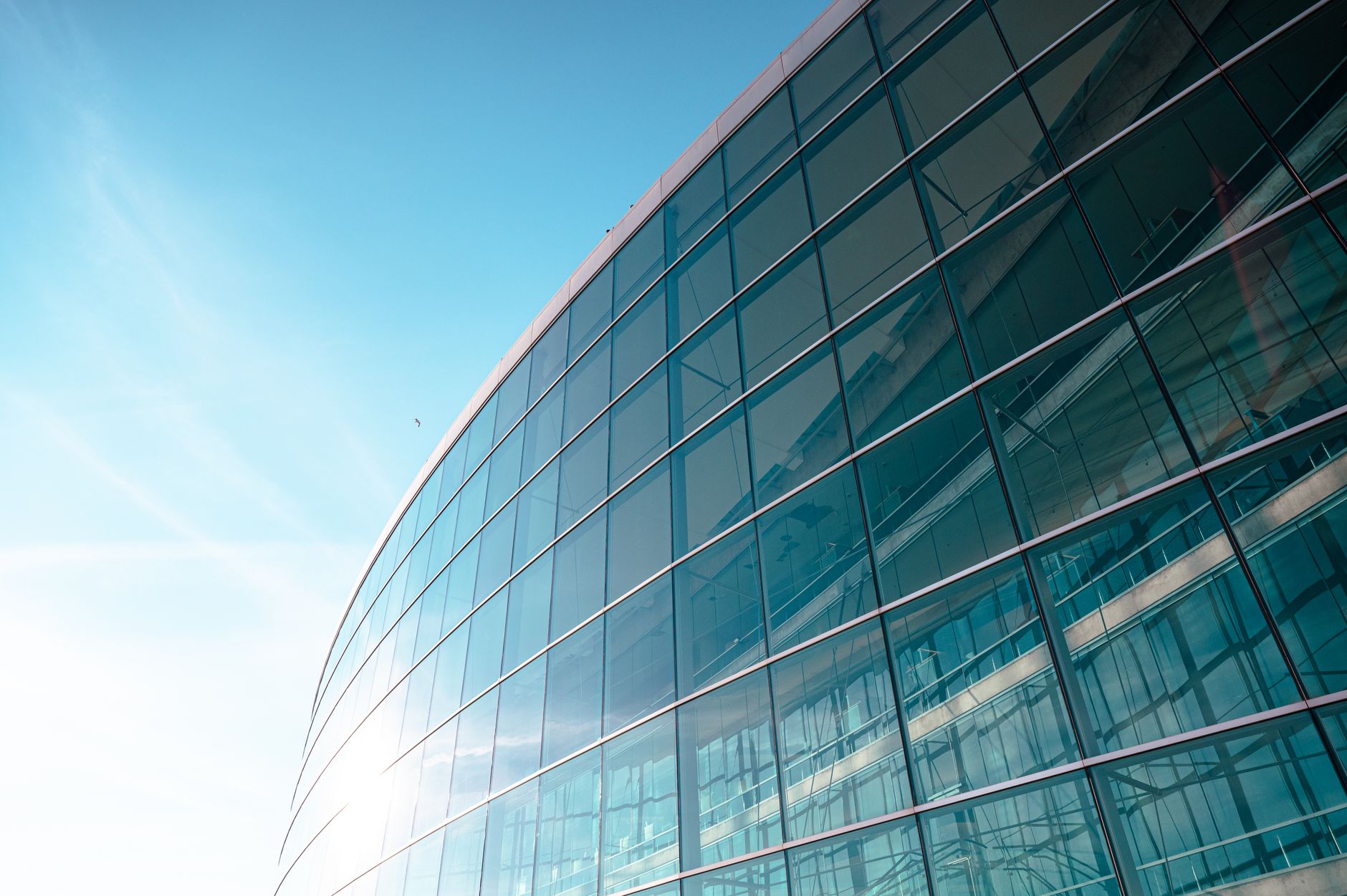 exterior of a modern glass-and-steel corporate campus with a large digital display showing software analytics dashboards, shot at midday under a clear sky