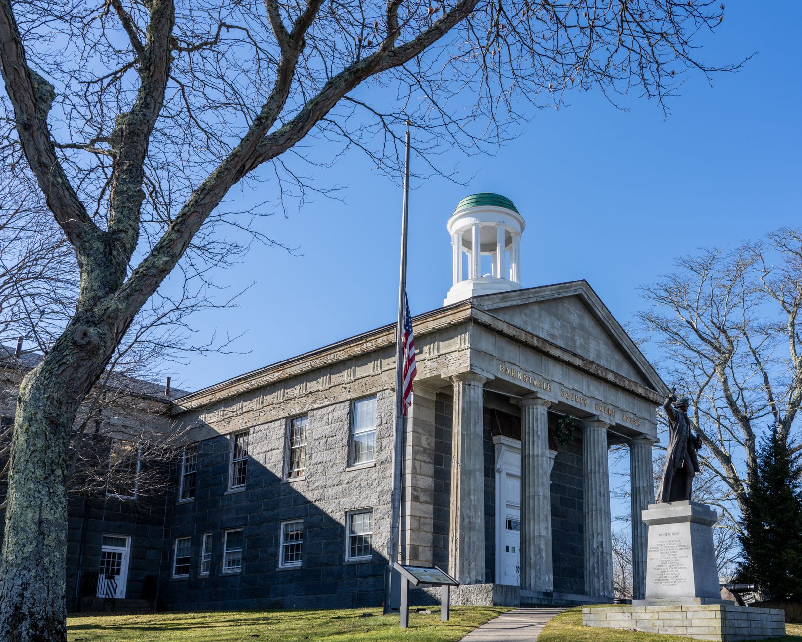 exterior of a U.S. federal government building with stone columns and a flagpole visible against an overcast sky