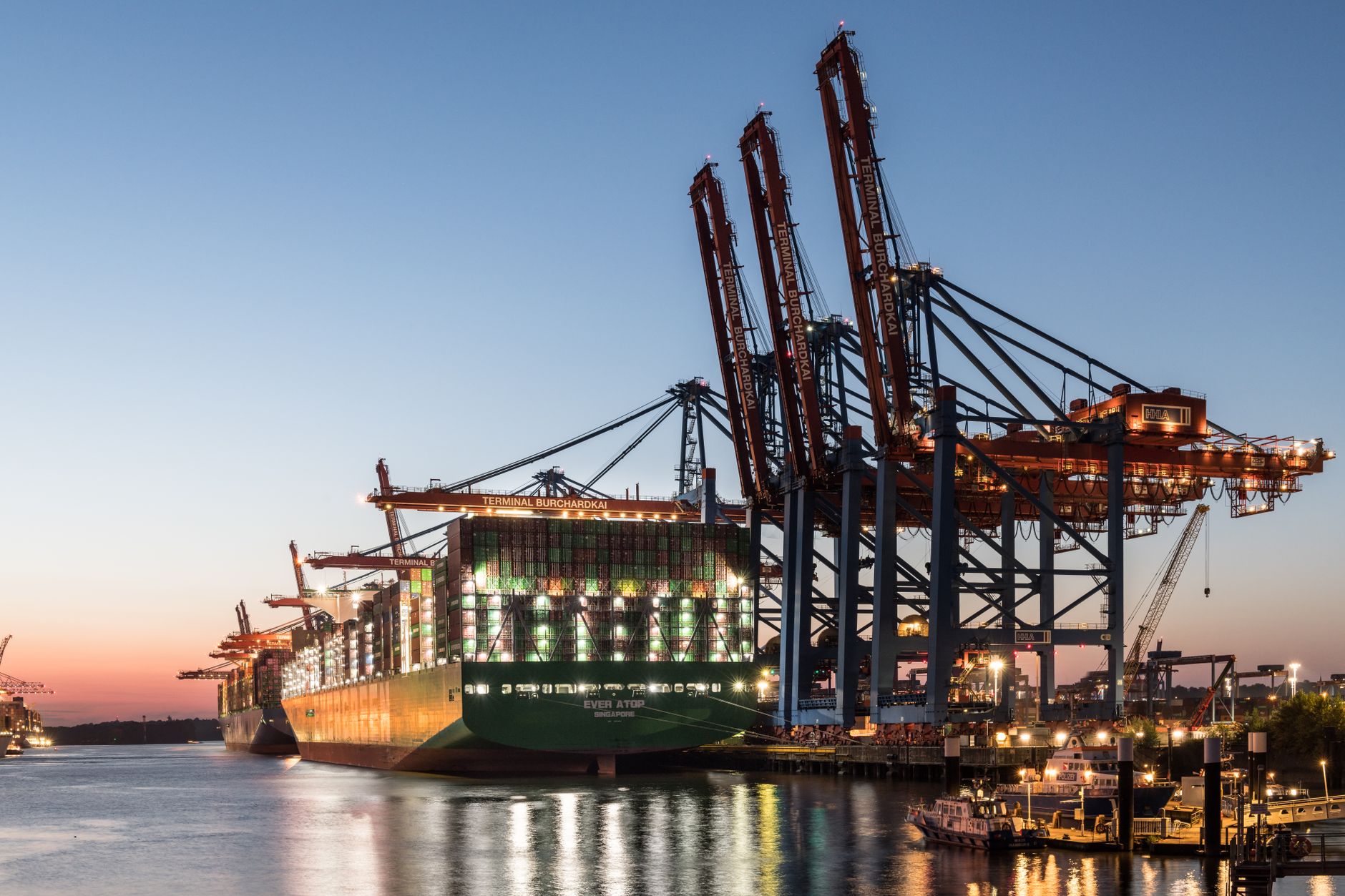 aerial view of a major Gulf port at dusk with container ships docked and cranes silhouetted against an orange sky