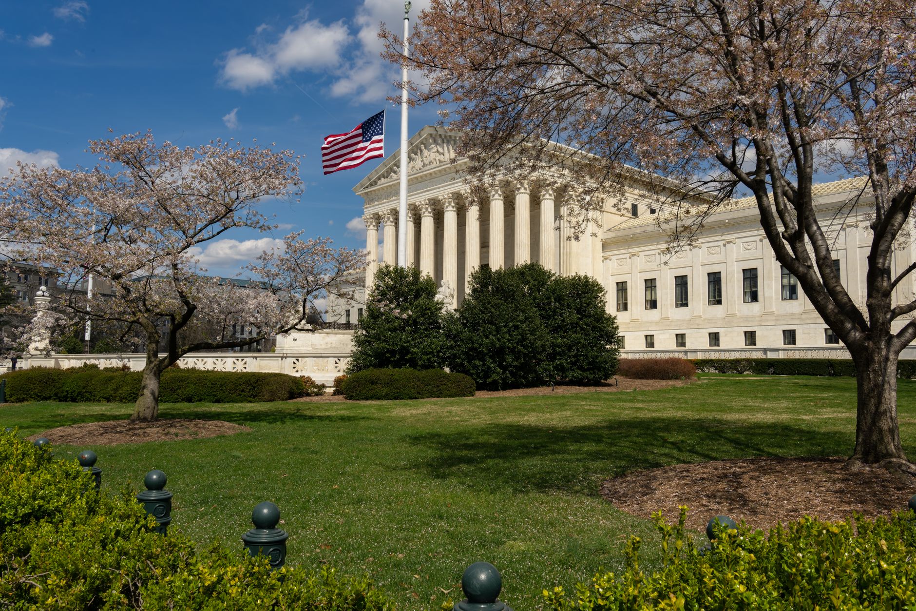 rows of empty courtroom wooden benches facing an elevated judicial bench inside a formal federal courtroom, American flag standing to the side