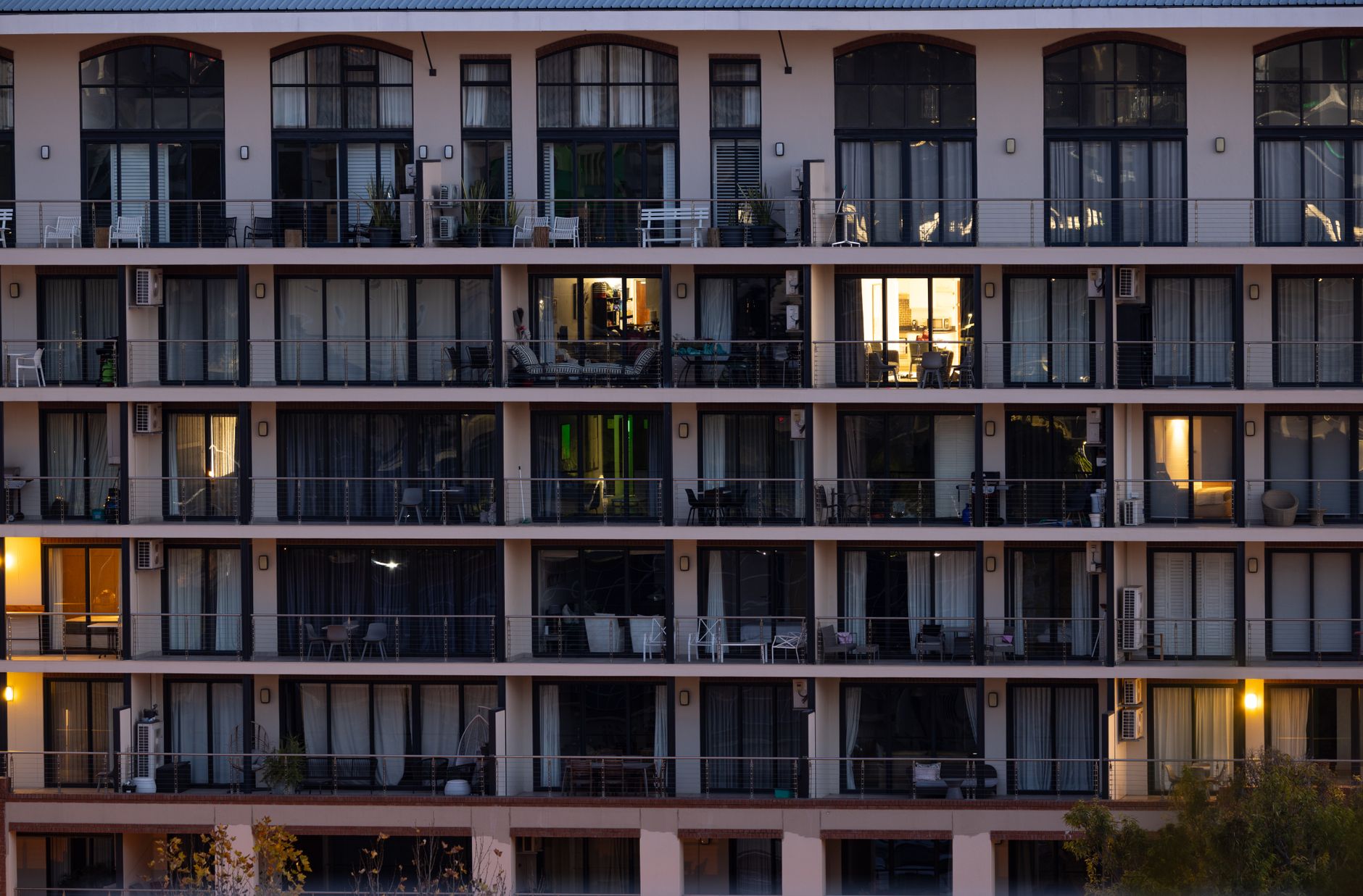 exterior of a modern glass-fronted biotech office complex at dusk, with interior lights illuminating open-plan research floors visible through floor-to-ceiling windows