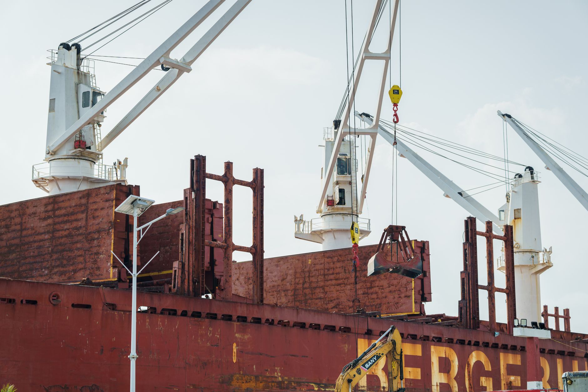 a modern naval patrol vessel moored at a Red Sea port facility, with cranes and storage tanks visible along the industrial quayside