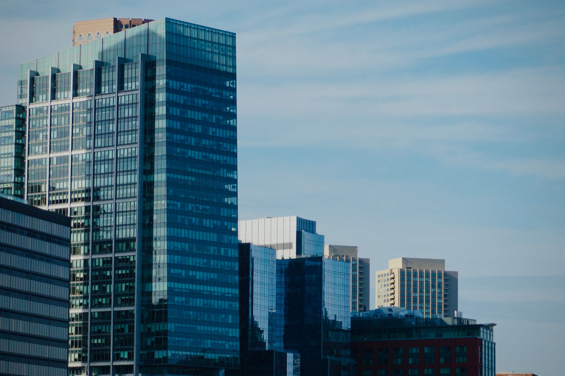 exterior of a modern financial services office building at midday, with glass facade reflecting clouds and a city skyline