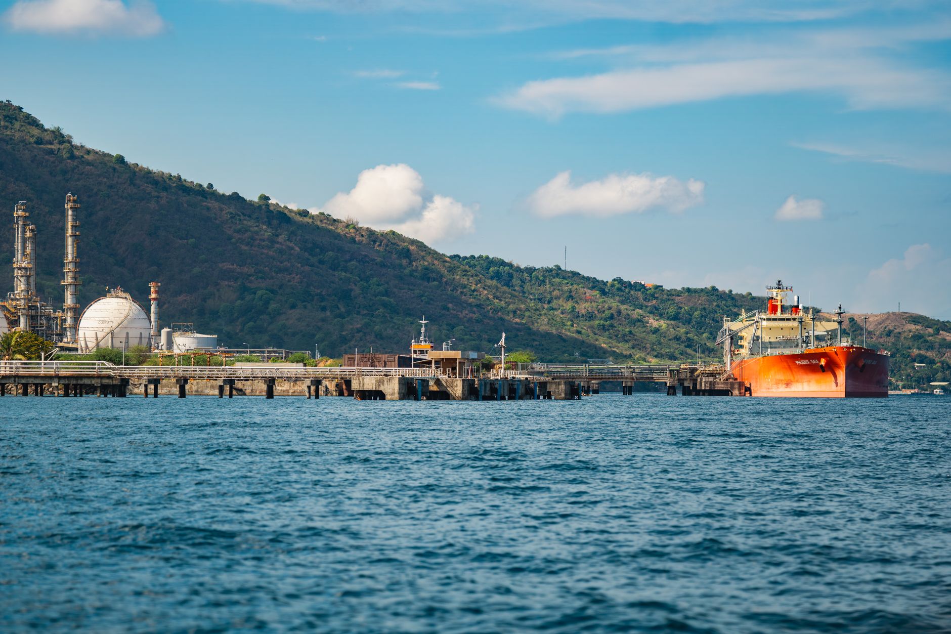 exterior view of a large oil terminal at dusk, with tankers visible on the water and industrial loading infrastructure in the foreground