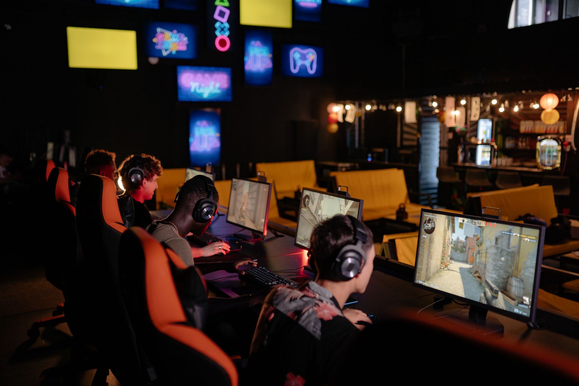 rows of desktop gaming computers in a dimly lit internet cafe in a Chinese city, screens displaying colorful online game interfaces