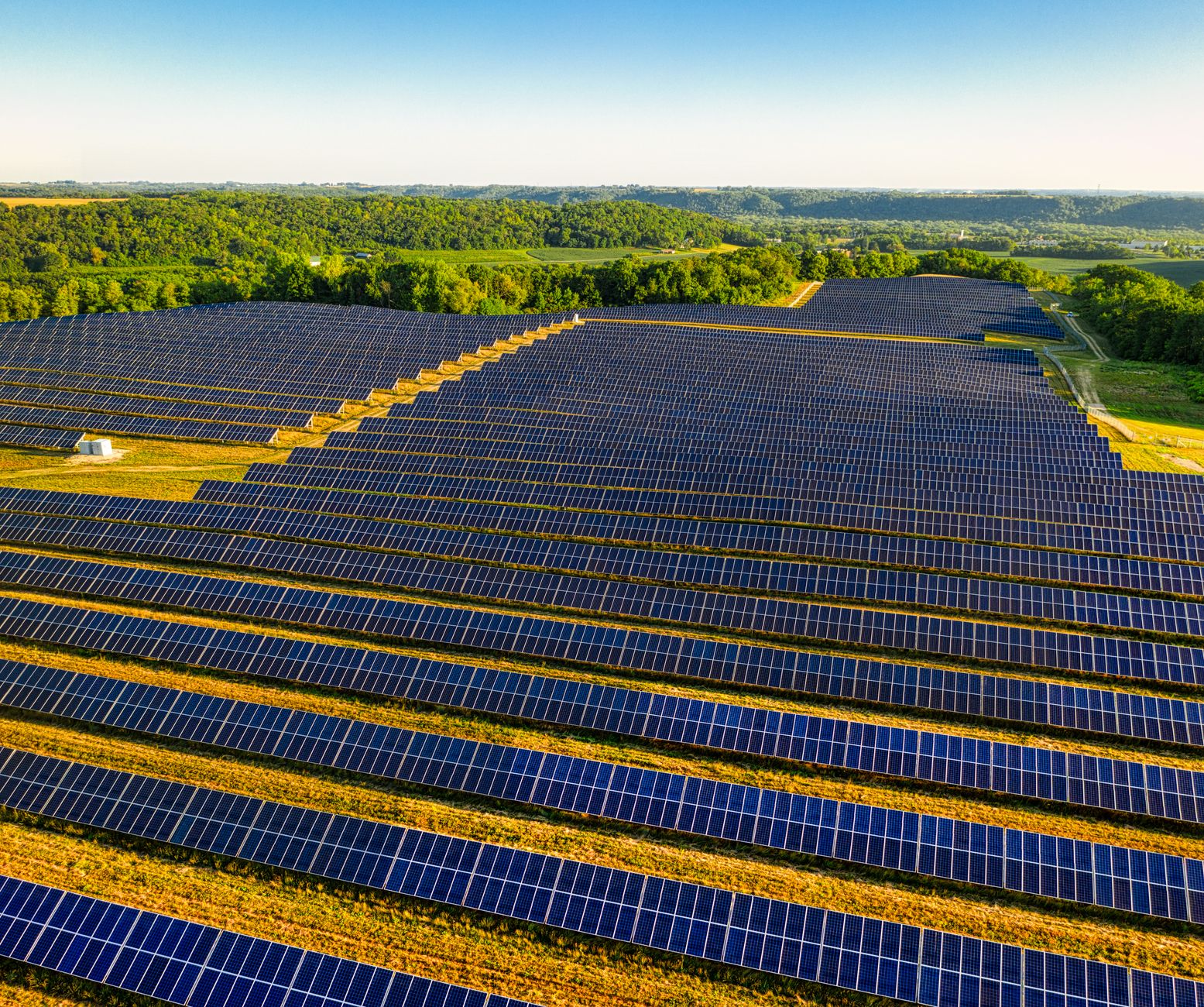 vast utility-scale solar farm with rows of photovoltaic panels stretching toward the horizon at golden hour, no people visible