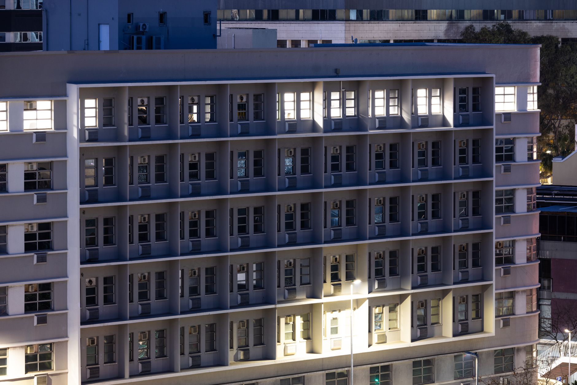 exterior of a multi-story tech campus building at dusk with illuminated windows and a reflection in a glass facade, set against a darkening sky