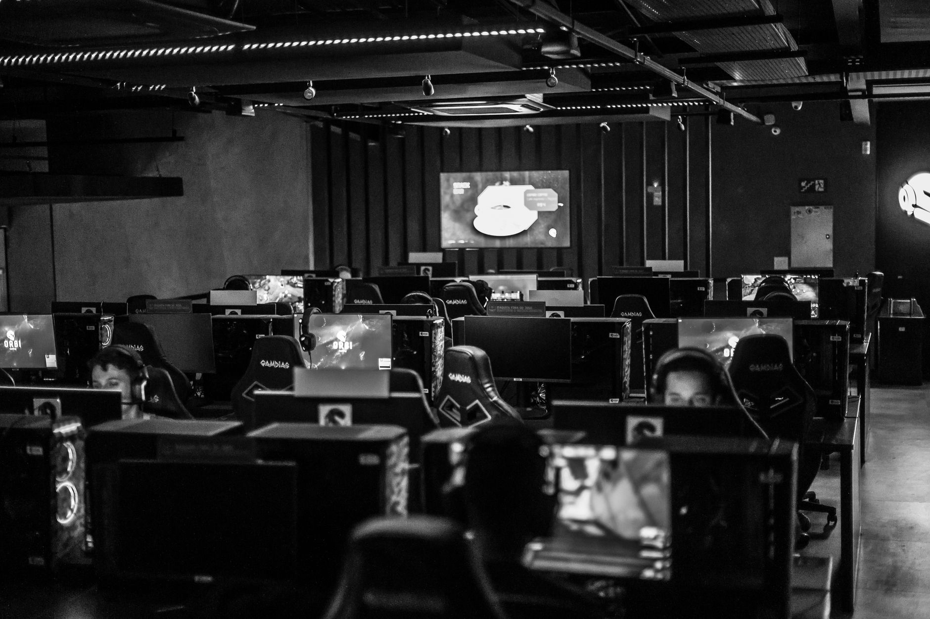 a darkened broadcast studio with multiple inactive computer monitors and empty gaming chairs arranged around a central streaming desk, overhead lights dimmed