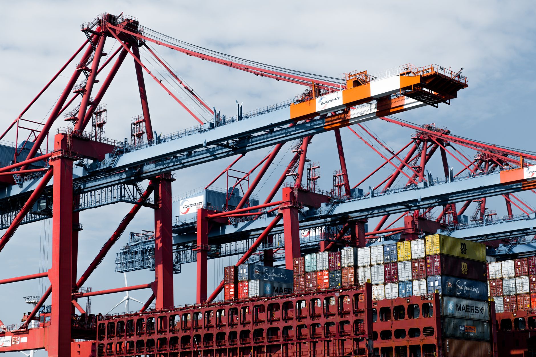 rows of shipping containers stacked at a busy commercial port under overcast skies, cranes visible in the background