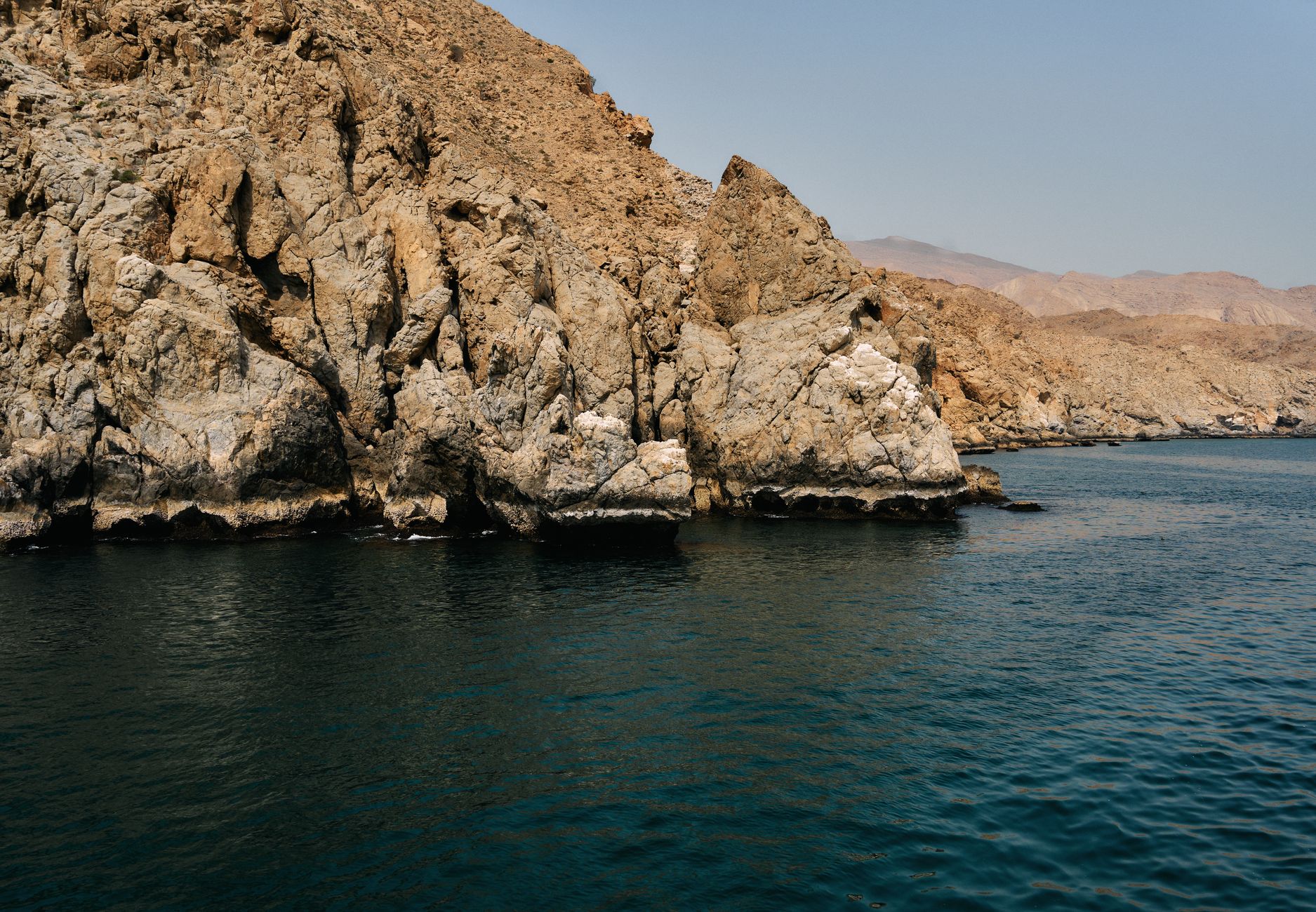 wide shot of a supertanker passing through a narrow sea channel flanked by rocky desert terrain
