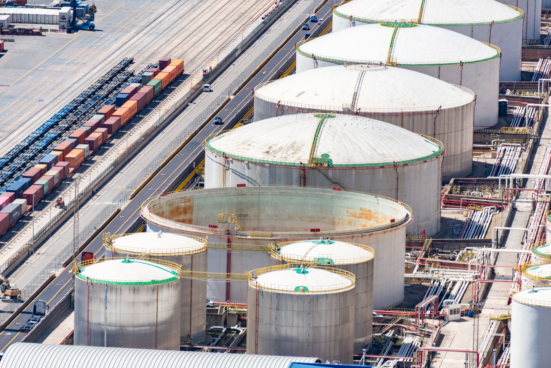 aerial view of a large oil refinery complex with industrial pipelines and storage tanks stretching across a coastal plain