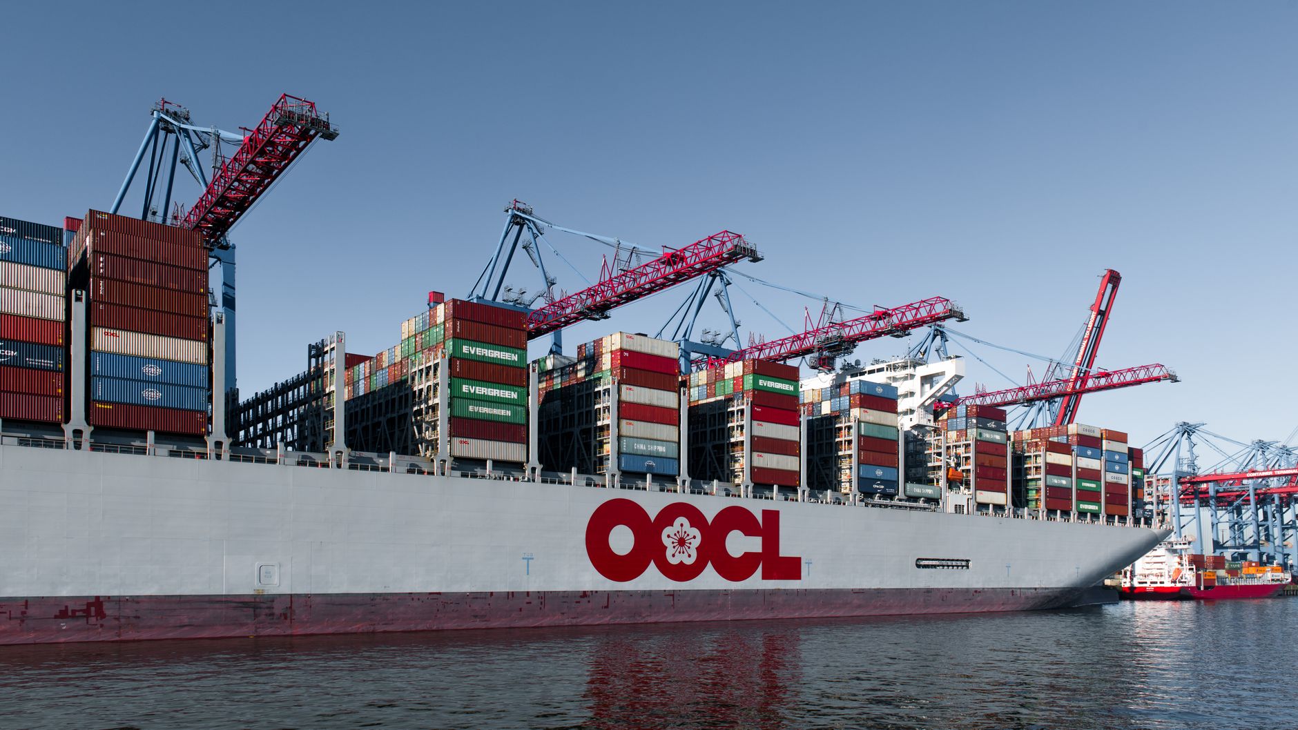 wide-angle exterior of a large commercial port with cranes and shipping containers, some infrastructure visibly damaged or inactive