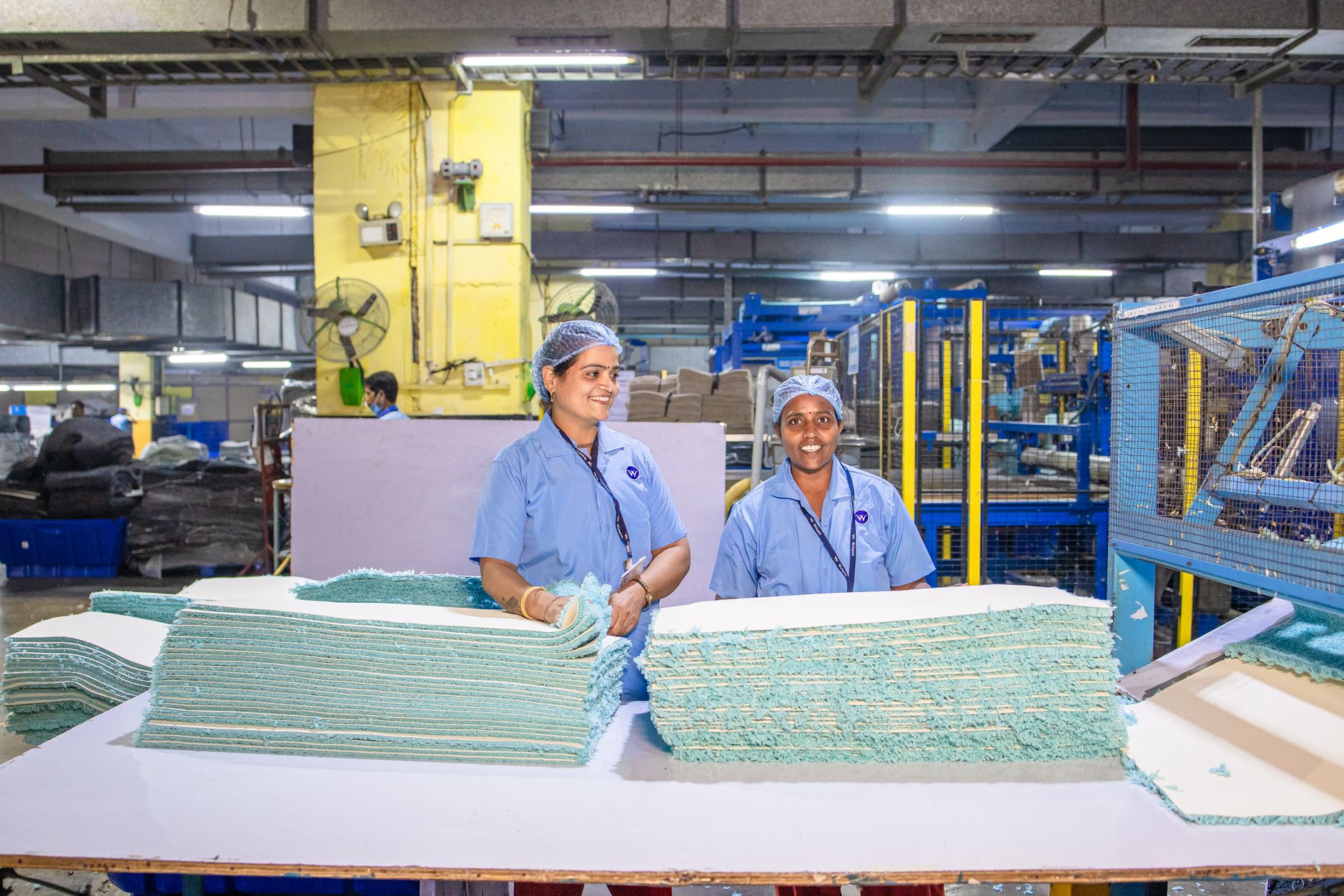 rows of blister-pack pharmaceutical production lines inside a large, fluorescent-lit Indian manufacturing facility, machinery in the foreground