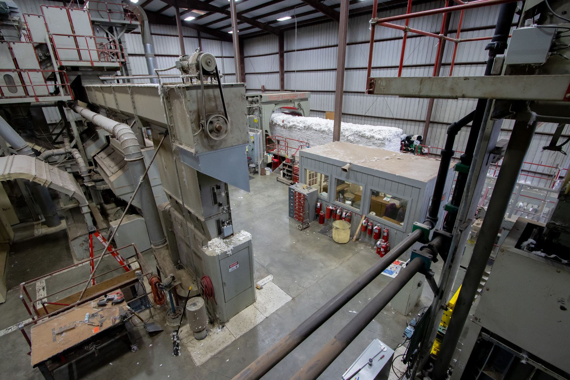 wide-angle view of a large American steel manufacturing plant interior, with industrial machinery and overhead cranes in operation, no workers as focal point
