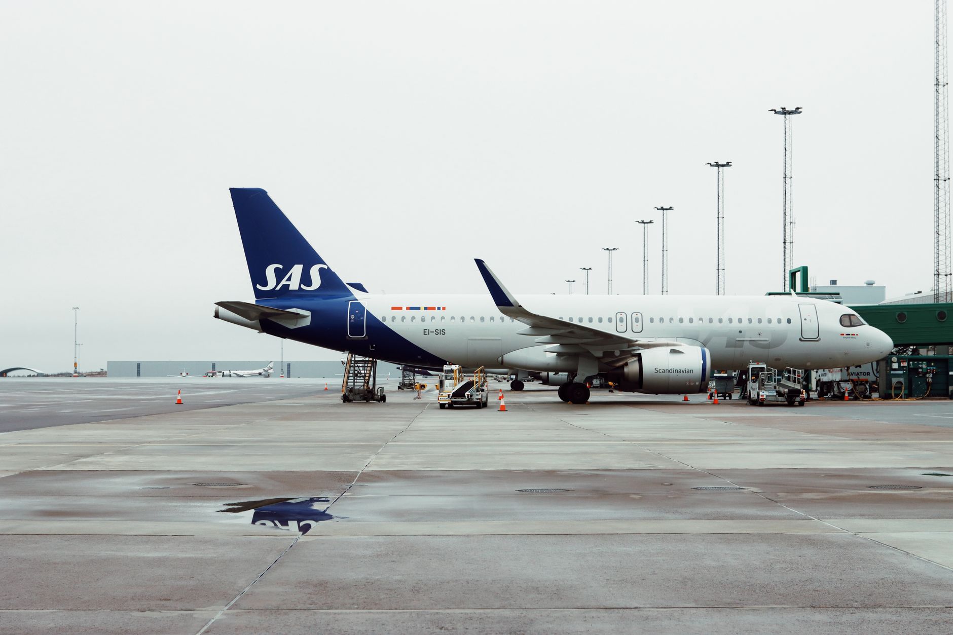 exterior of a commercial aircraft on a tarmac at an international gateway airport, with ground service equipment positioned nearby and an overcast sky above