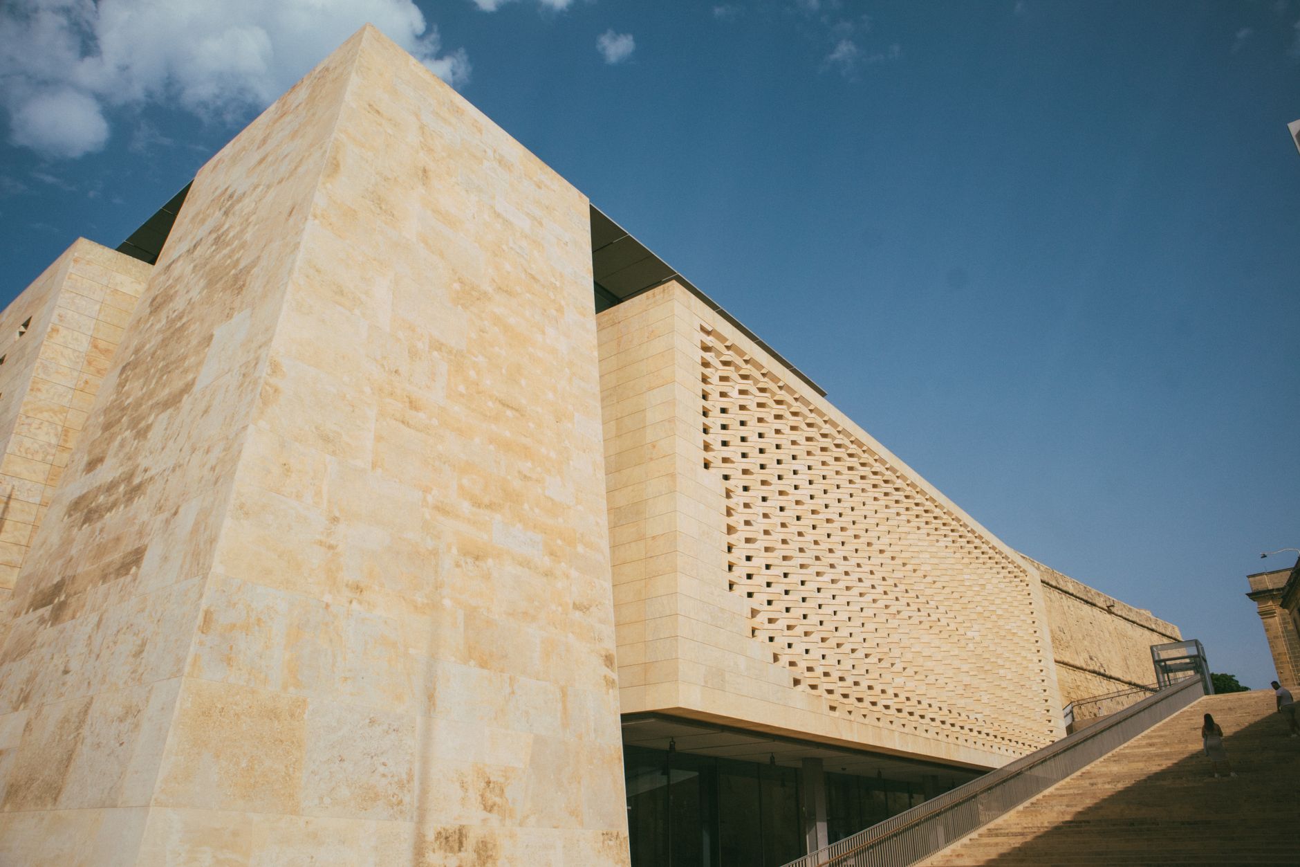 exterior of the Israeli Knesset building at midday, stone facade and flagpoles visible against a pale blue sky