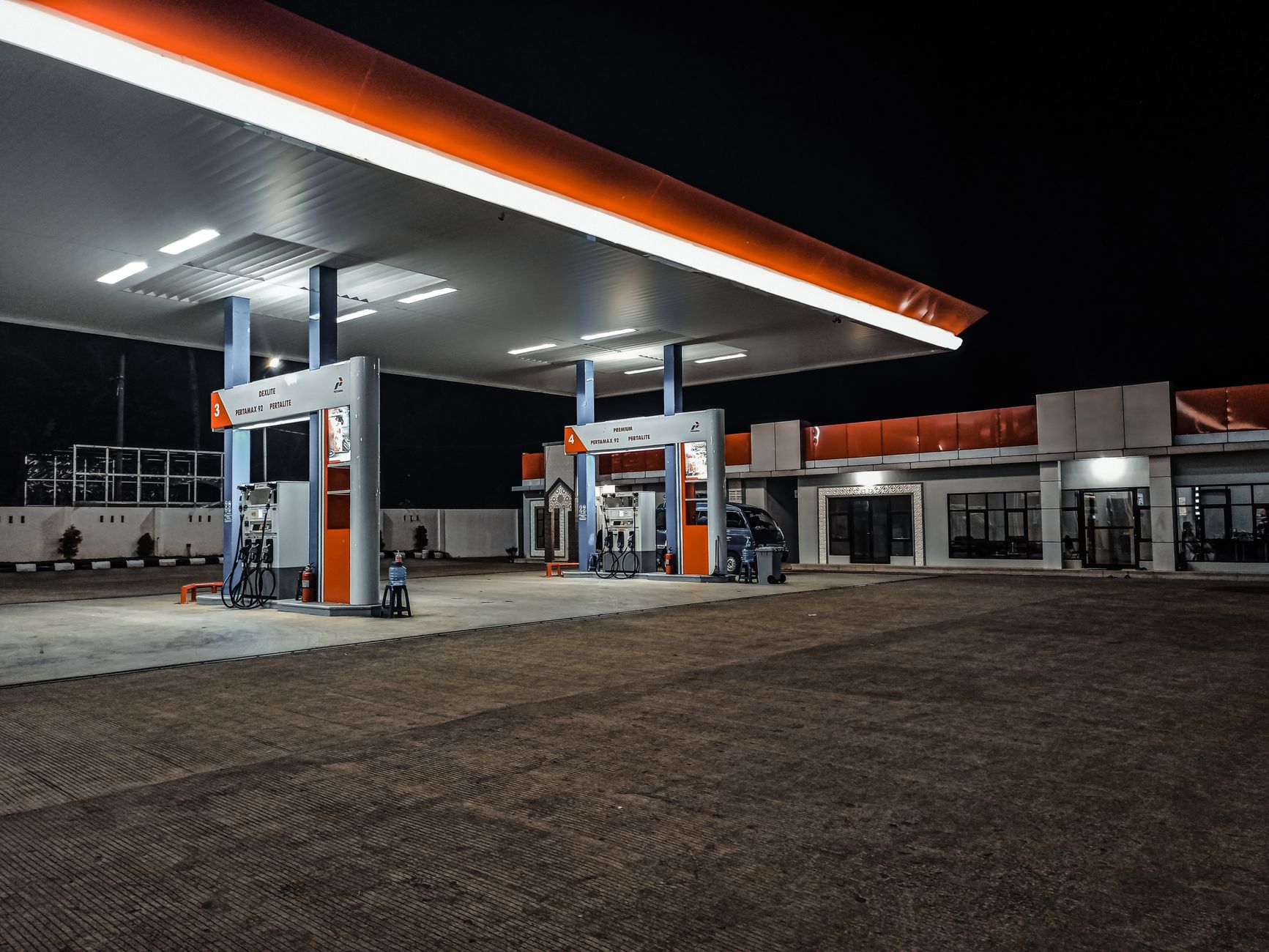 exterior of a large suburban grocery store with a fuel station forecourt in the foreground, price signage visible on the pump canopy