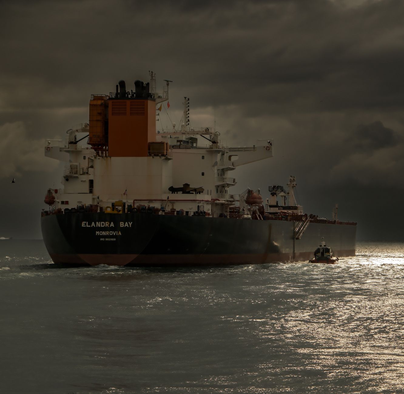 aerial view of a large oil tanker navigating through a narrow sea passage at dusk, with calm waters reflecting fading light