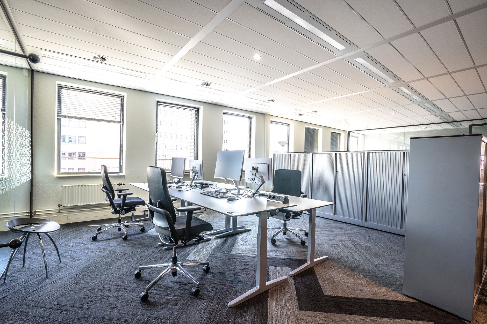 rows of empty office workstations in a large open-plan corporate floor, natural light coming through floor-to-ceiling windows