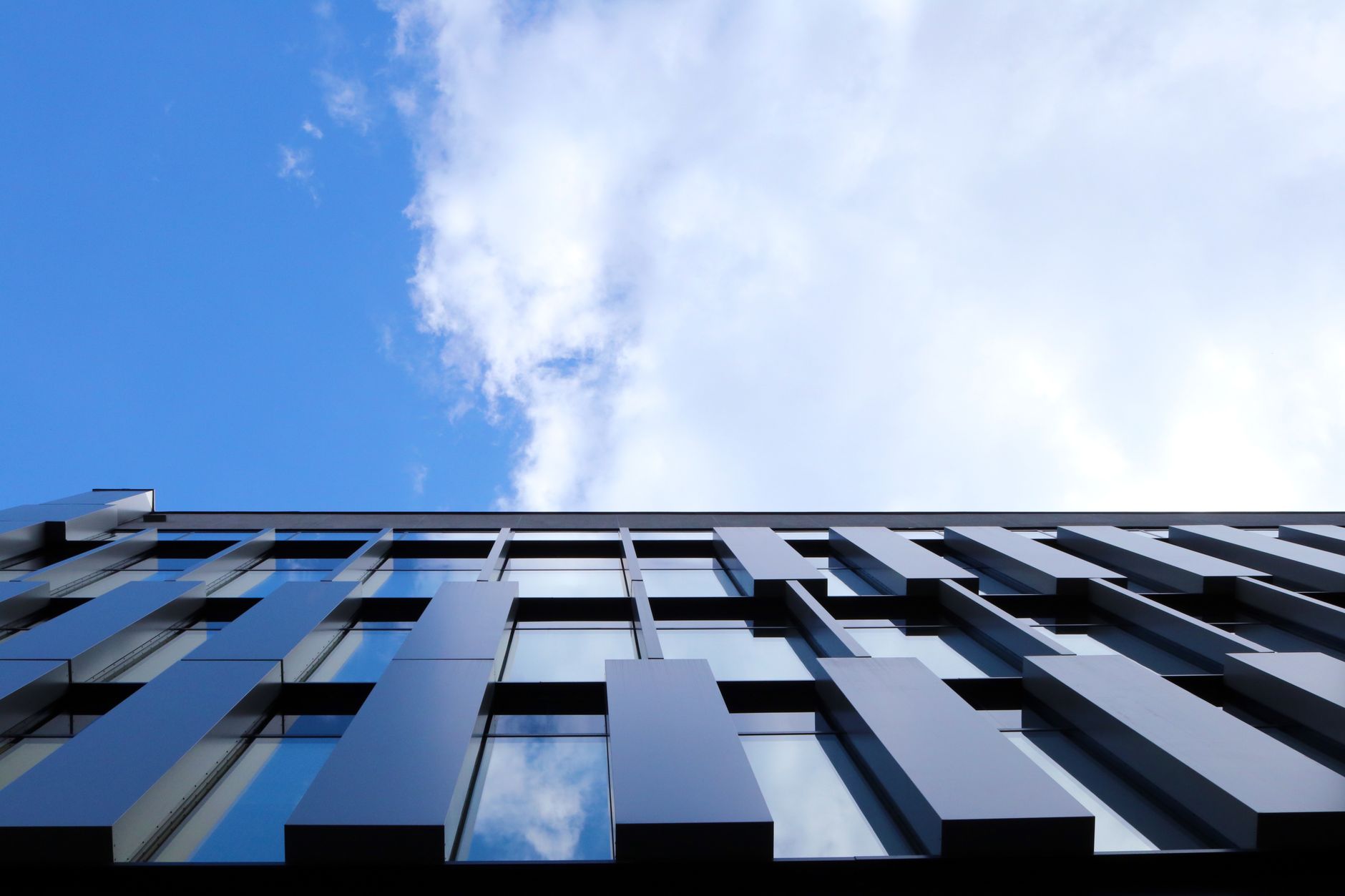 exterior of a glass-fronted technology office building in an urban business district at late afternoon, reflecting nearby city skyline