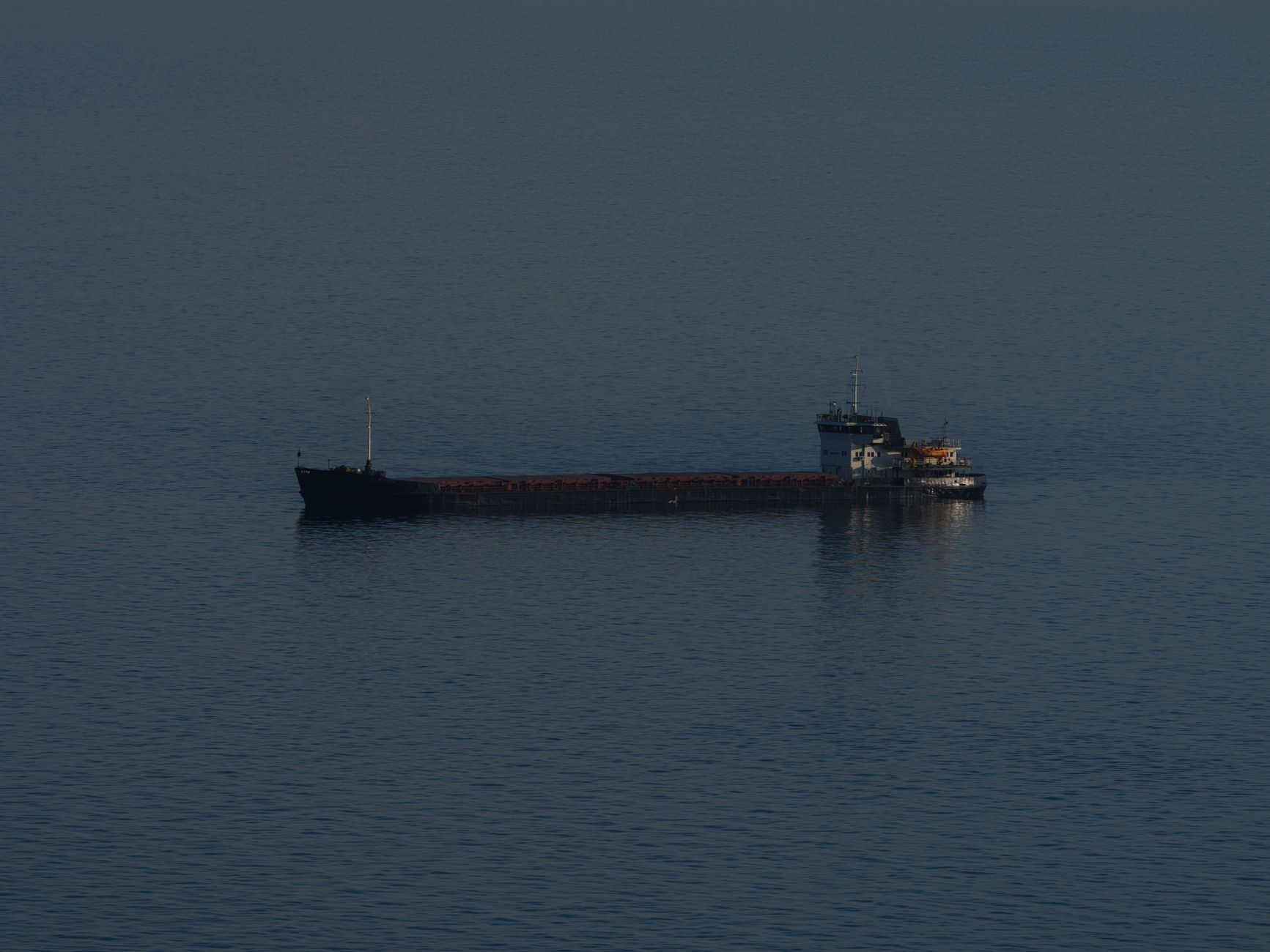oil tanker vessel anchored in open sea under an overcast sky, viewed from an elevated angle showing deck infrastructure