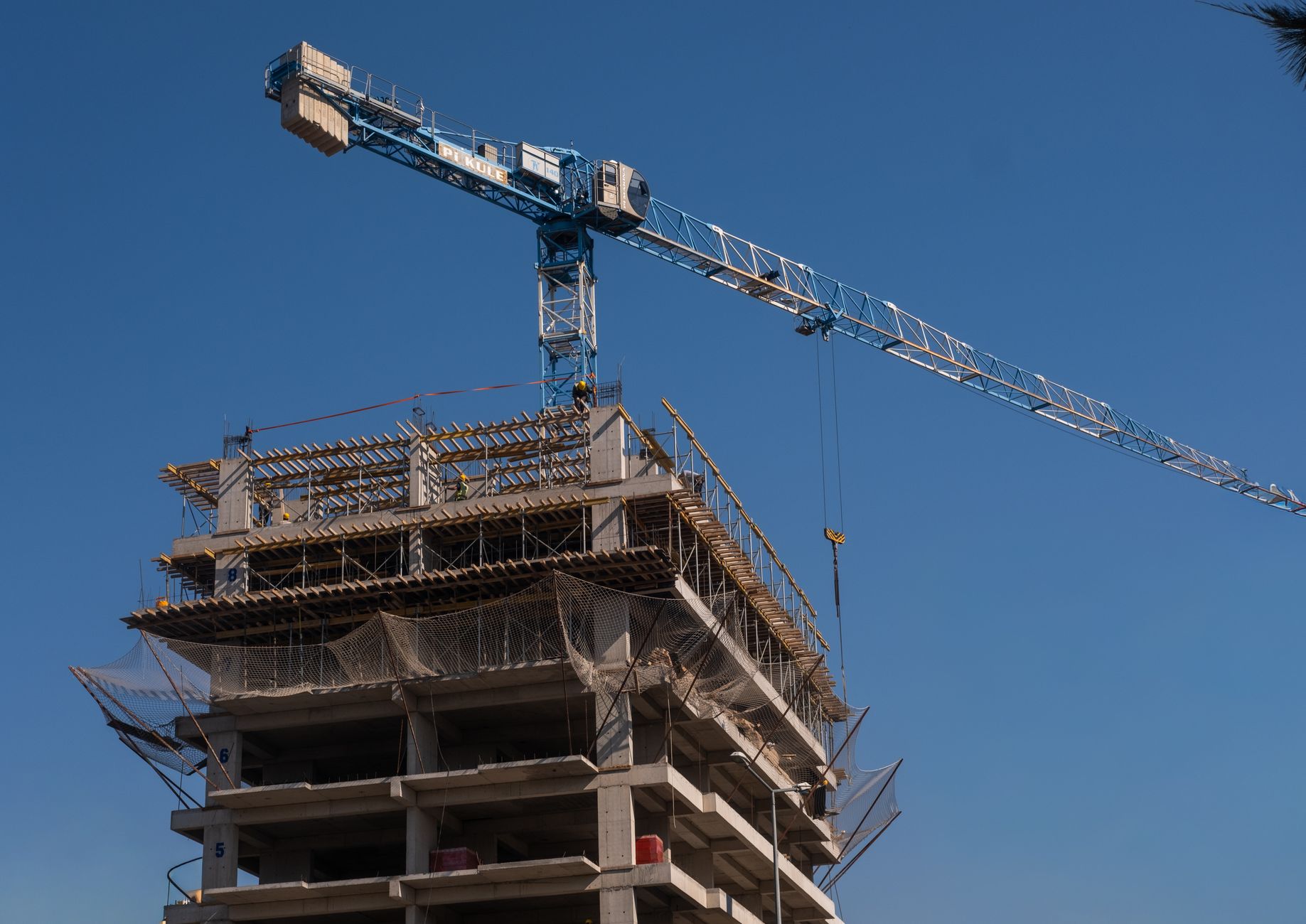aerial view of a large active construction site with cranes, scaffolding, and partially completed concrete structures under clear daylight
