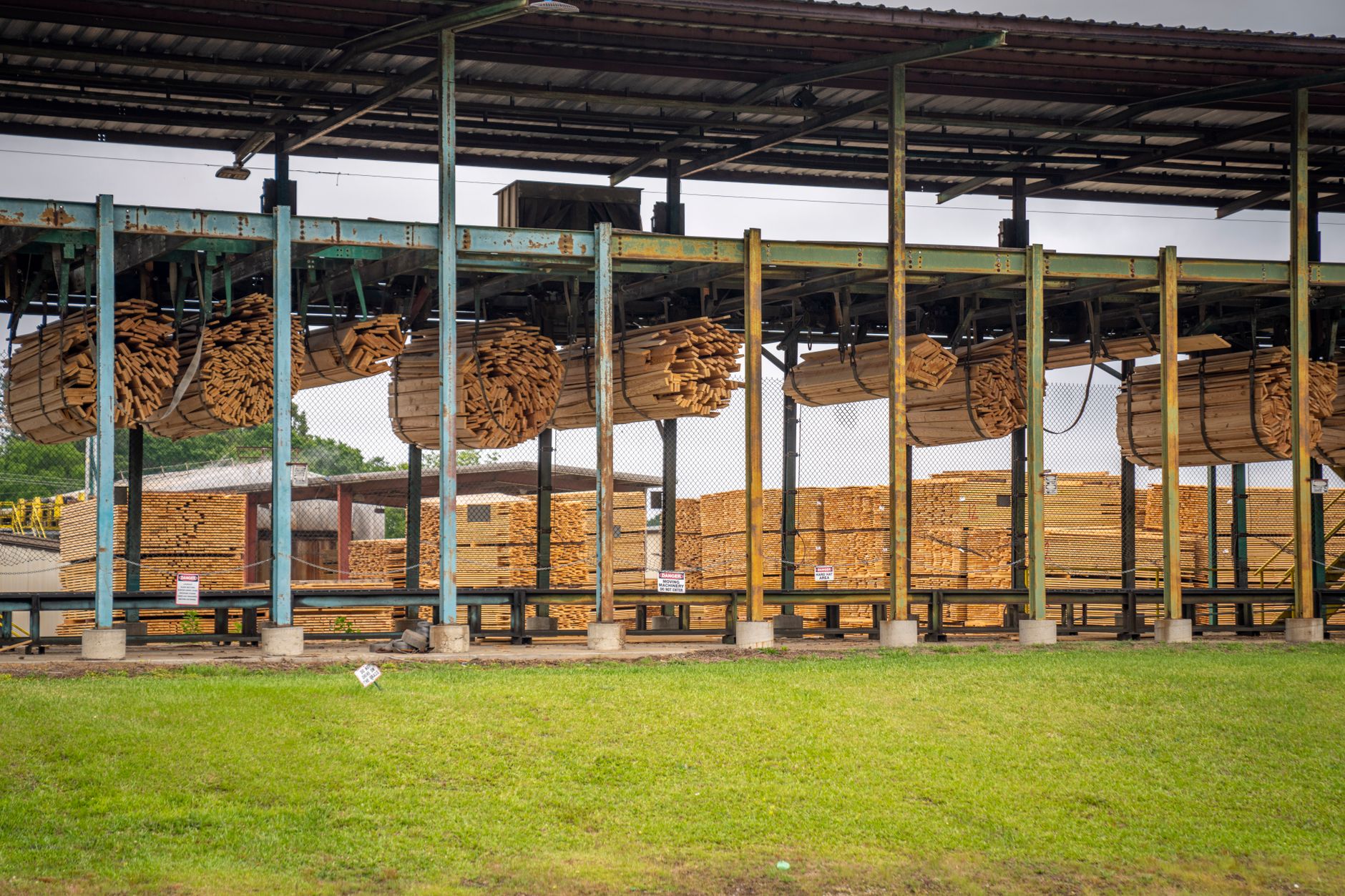 Wide shot of a large paper pulp processing facility in a forested region, with massive rolls of raw pulp stacked outside under a grey sky
