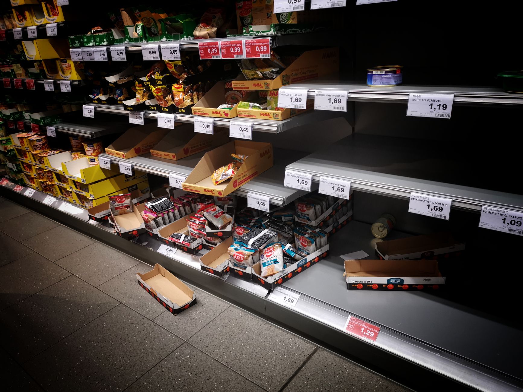 Mostly empty shelves in a supermarket's paper goods aisle, with only a few remaining packages of tissue products scattered across the racks