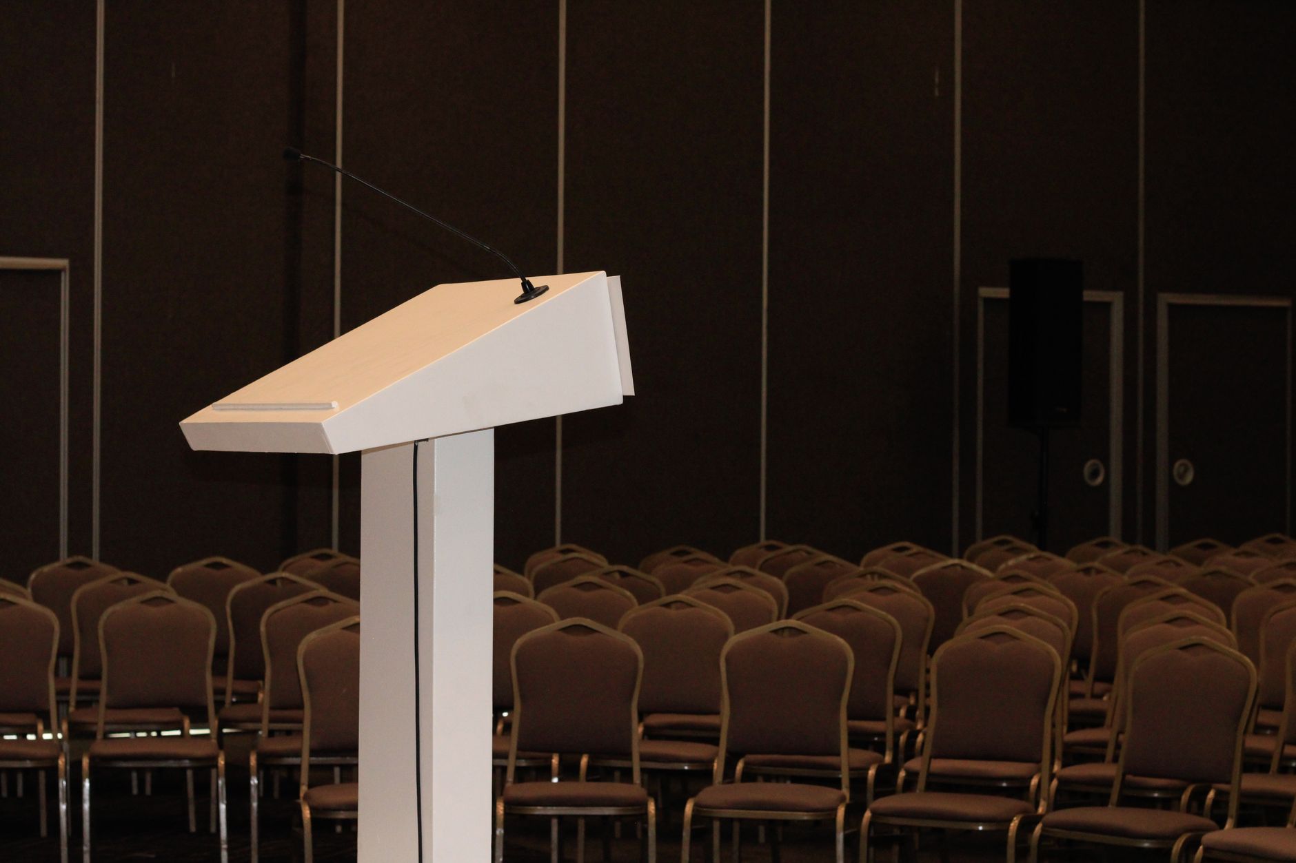 empty campus auditorium with rows of unoccupied seats and a podium lit by a single overhead light, no text or signage visible