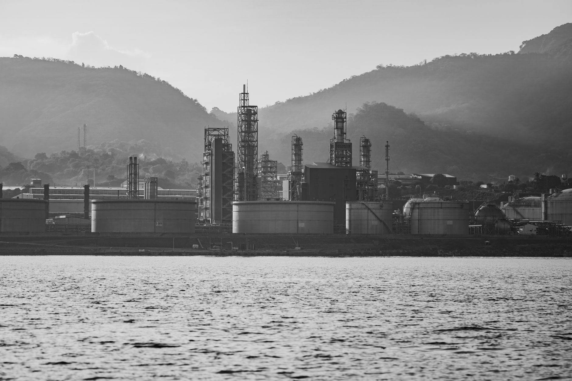 aerial view of an oil refinery complex along a river at dusk, with processing towers and storage tanks illuminated