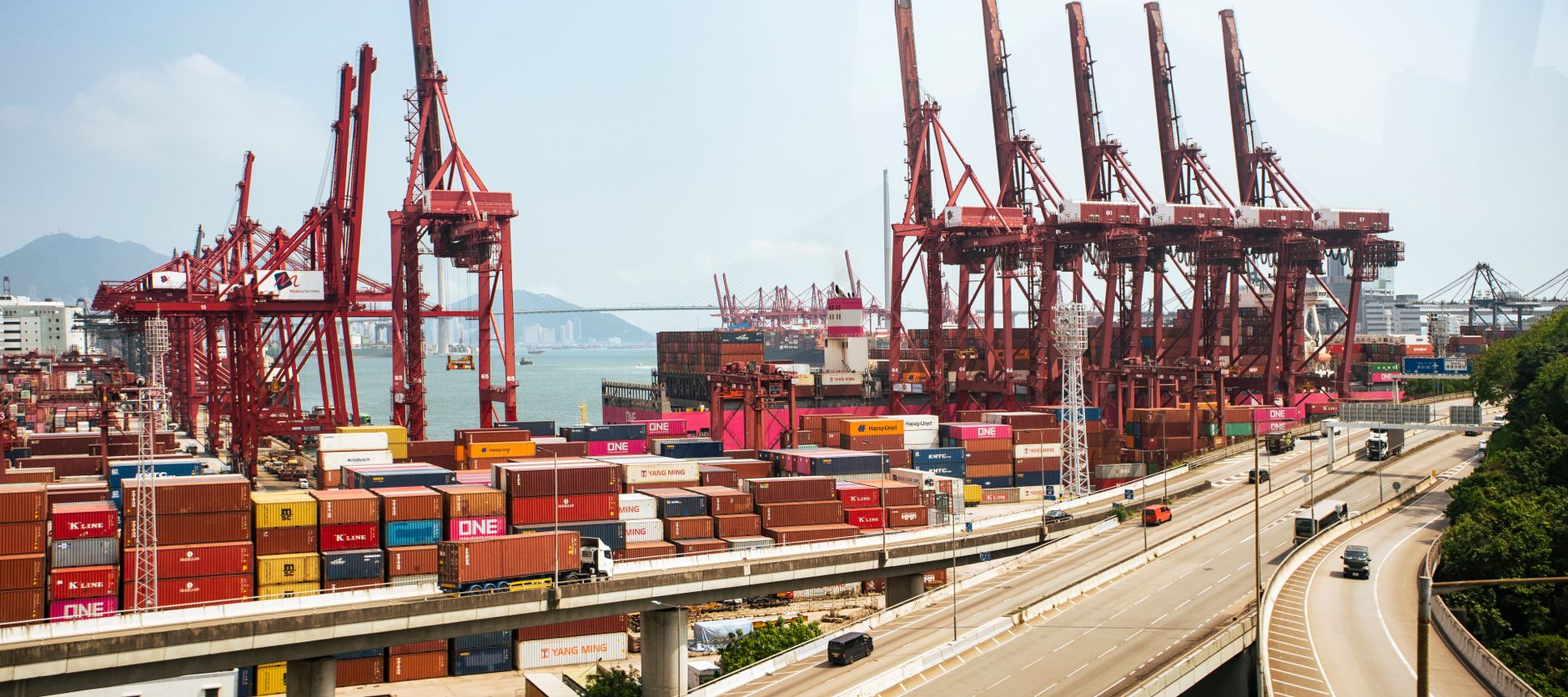 wide-angle view of a major Chinese container port at dawn, rows of stacked shipping containers stretching toward the horizon with cranes silhouetted against an orange sky