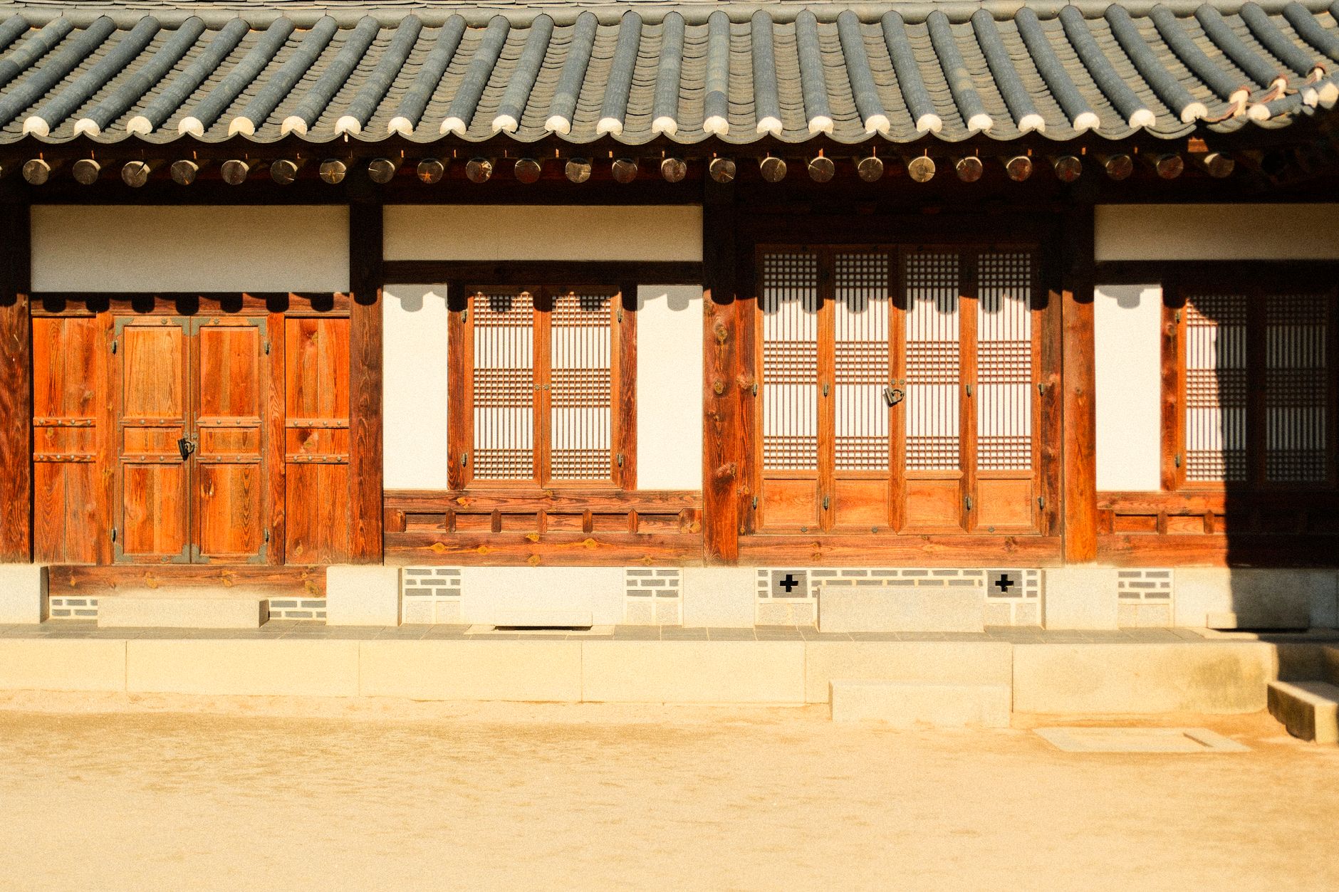 a traditional Korean farmhouse with wooden beams and a tiled roof surrounded by vegetable plots and stacked agricultural equipment in the foreground