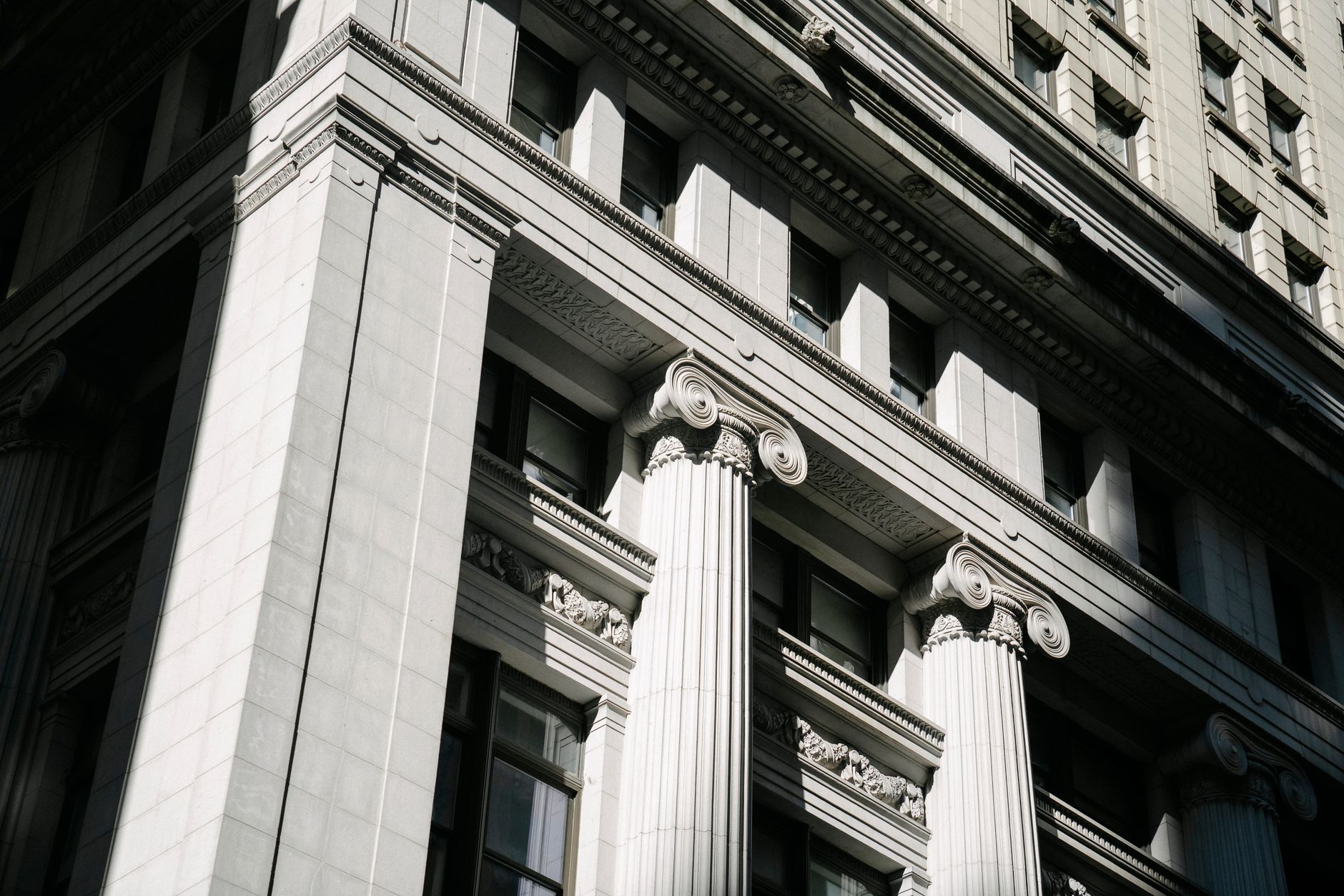 close-up of a bank branch exterior facade with stone columns and a glass entry door, afternoon light casting long shadows on the pavement