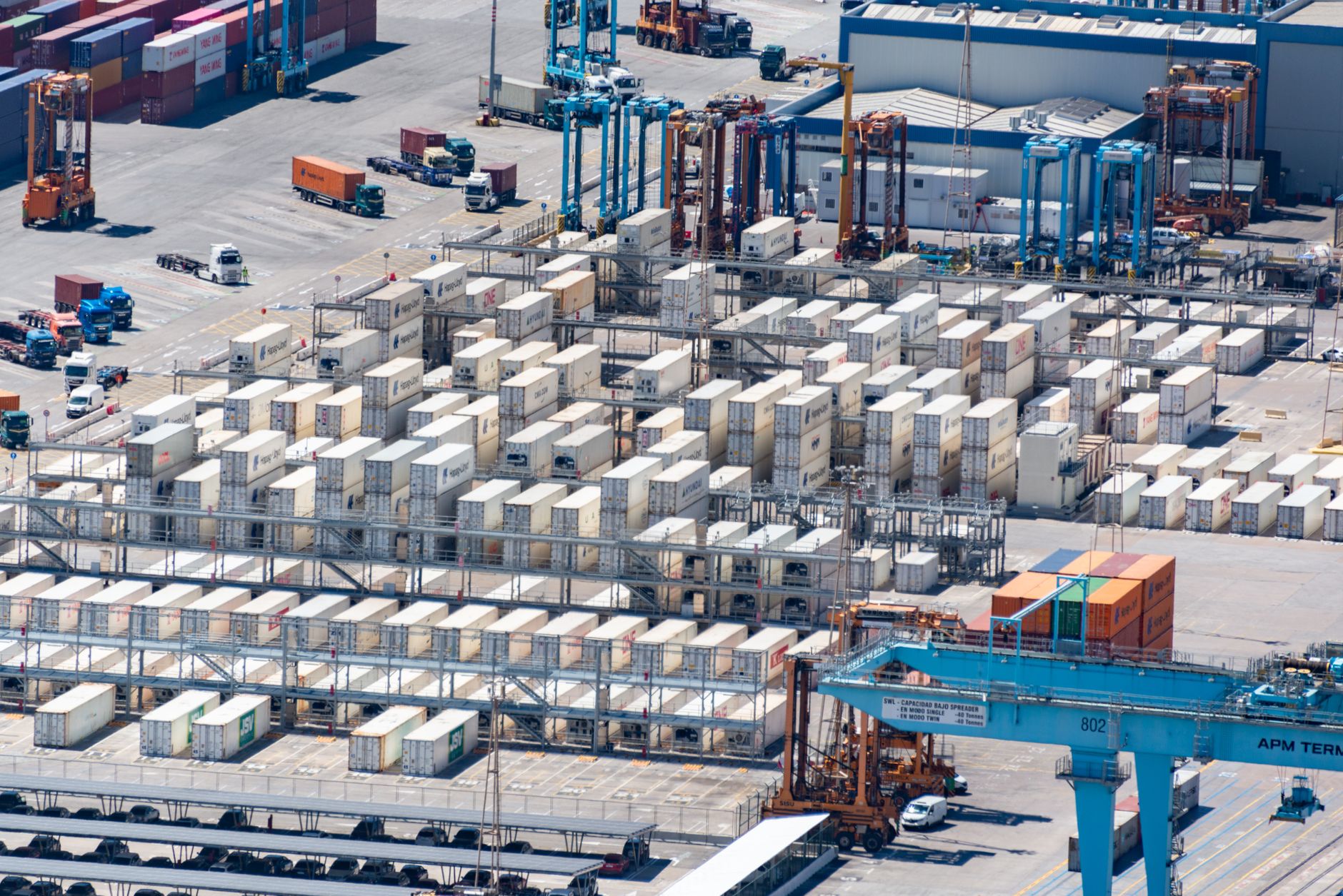 aerial view of a large container port with rows of stacked shipping containers and cranes along the quayside at midday