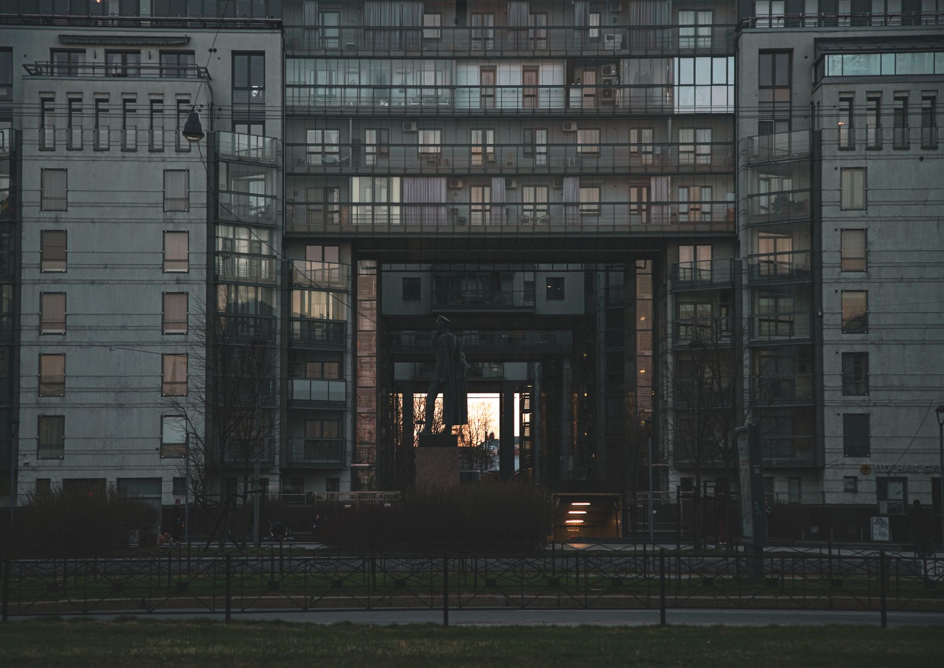 exterior facade of a large nonprofit hospital complex at dusk, illuminated signage visible above the main entrance, street-level ambulance bay in foreground