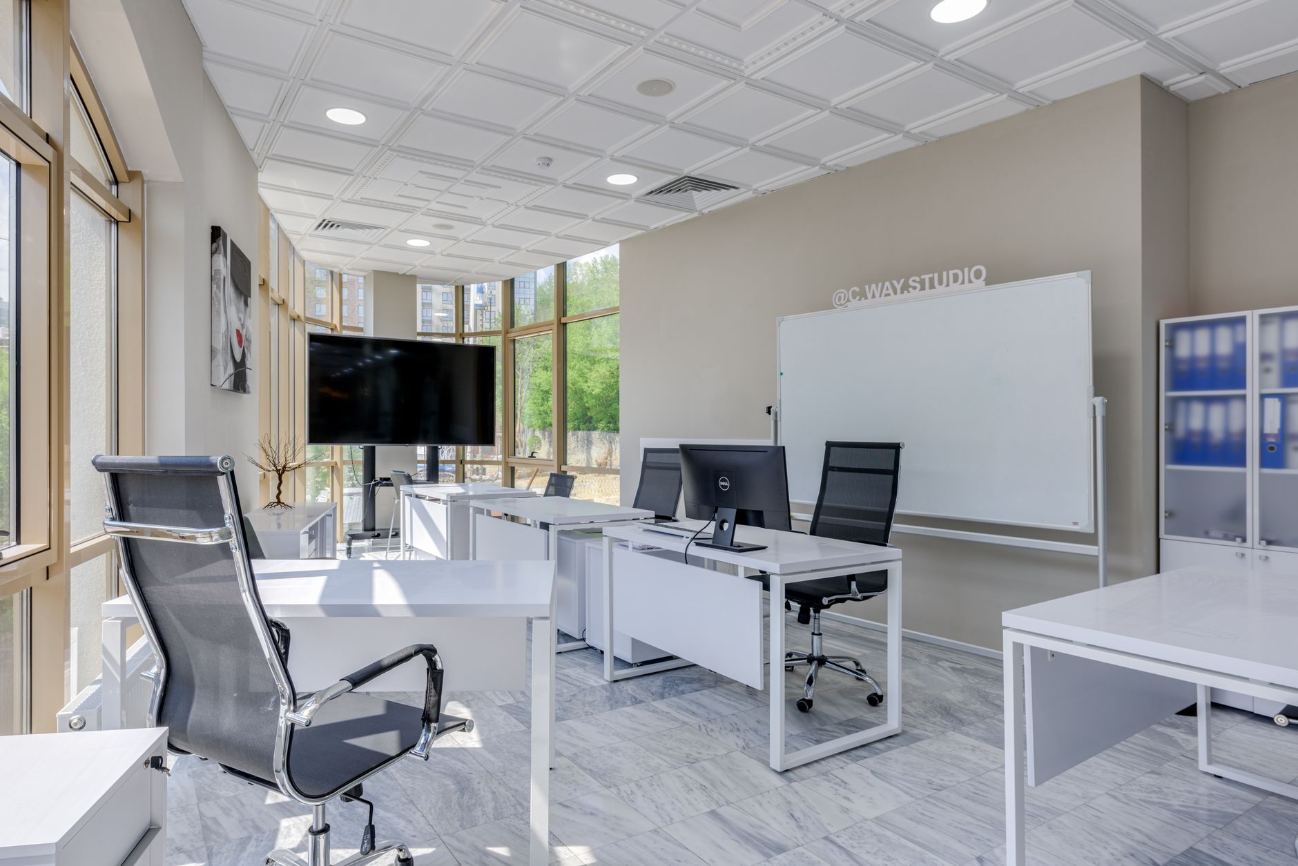 modern open-plan office interior with rows of standing desks, large wall-mounted monitors displaying dashboard interfaces, natural light from floor-to-ceiling windows