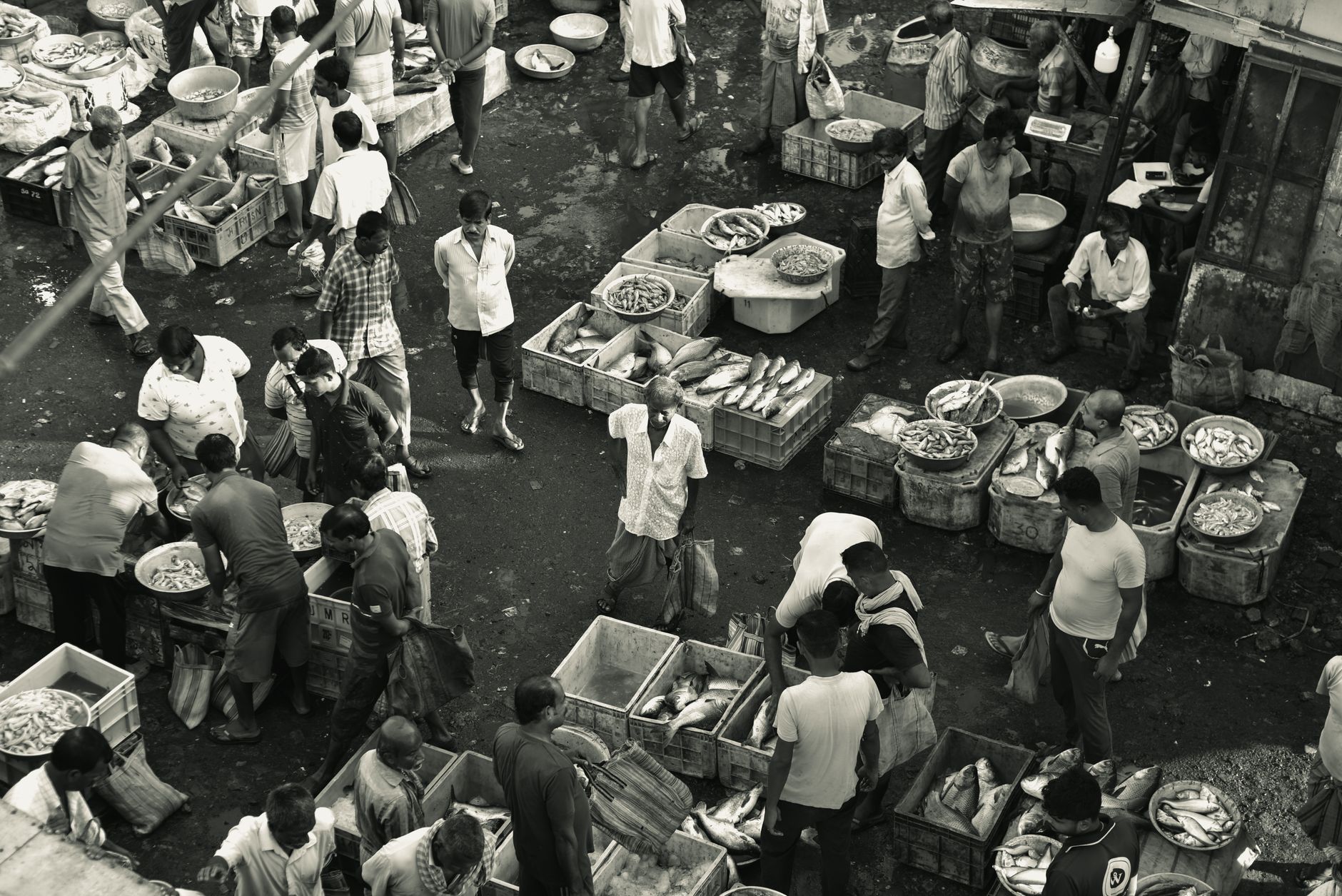 a busy street-level market in a mid-tier Indian city, with vegetable stalls and two-wheelers parked along a dusty road, shot from an elevated angle showing the density of commercial activity