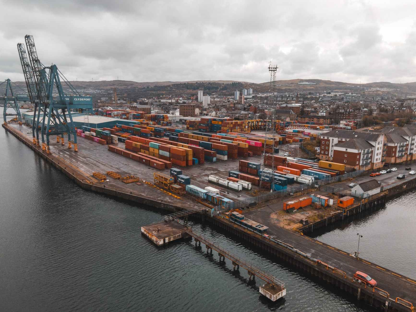 aerial view of a busy commercial port with cargo containers stacked in rows, cranes visible against an overcast sky