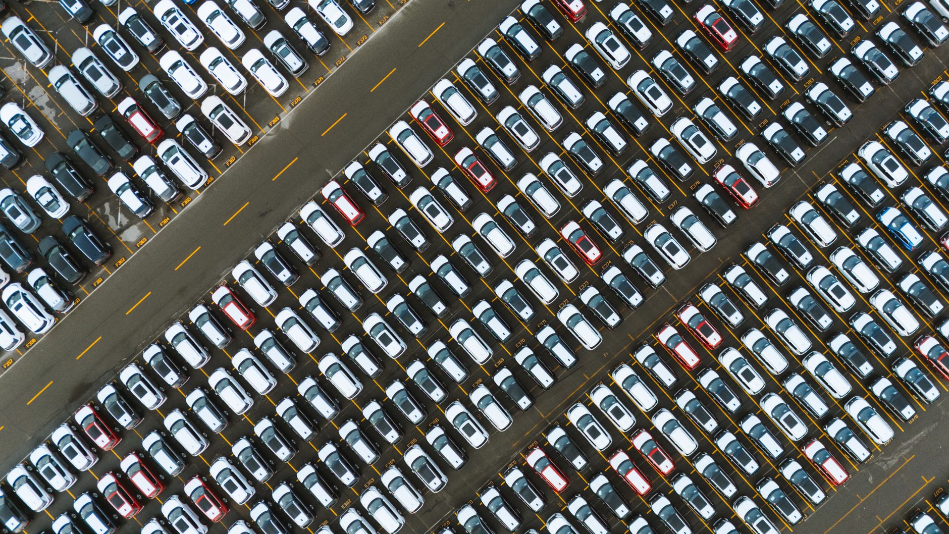 exterior of a new car dealership lot at dusk, rows of vehicles parked under overhead lights with price placards on windshields
