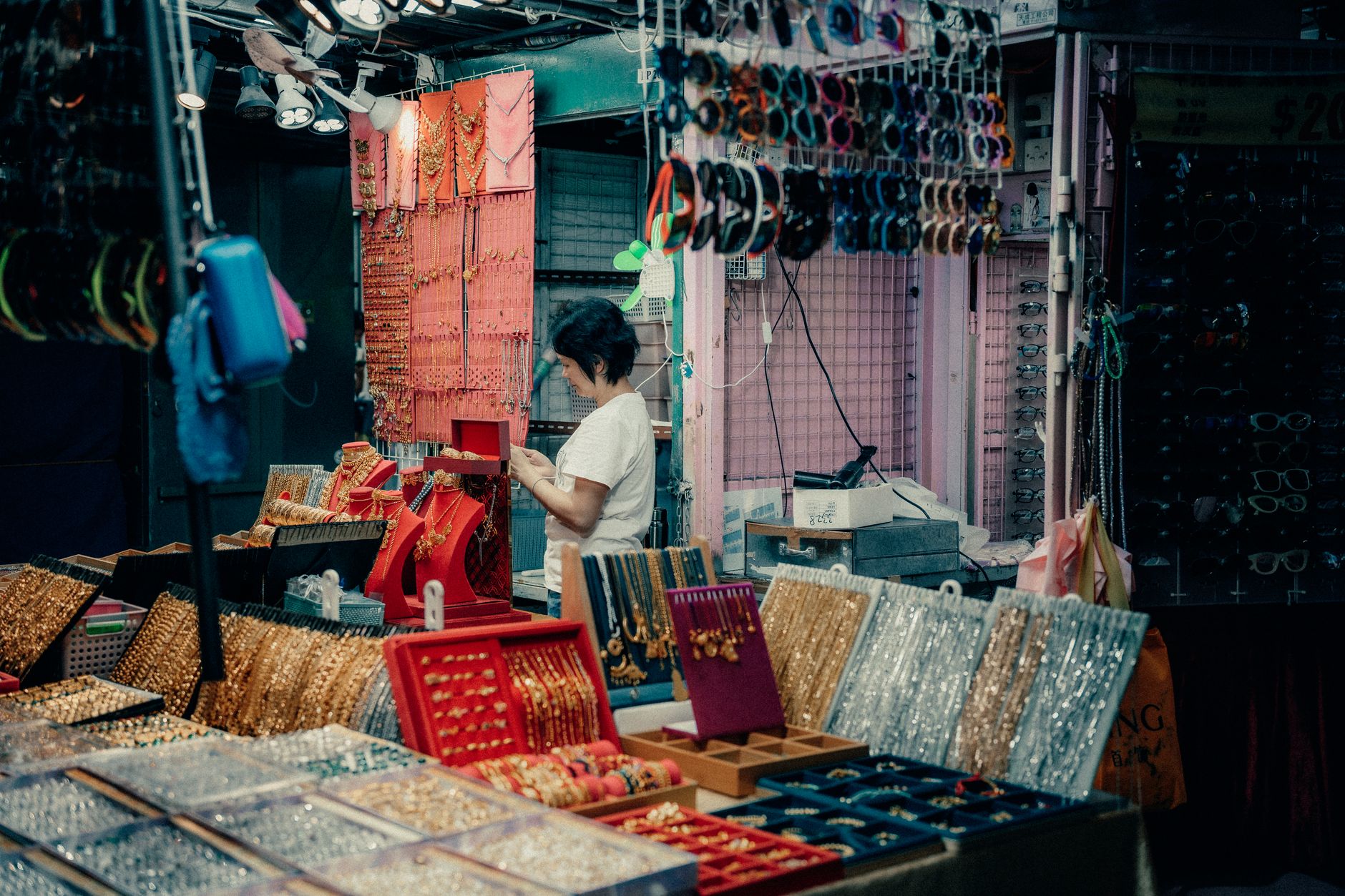 rows of gold coin display cases inside a Tehran jewelry bazaar, empty of customers, overhead lighting reflecting off glass surfaces