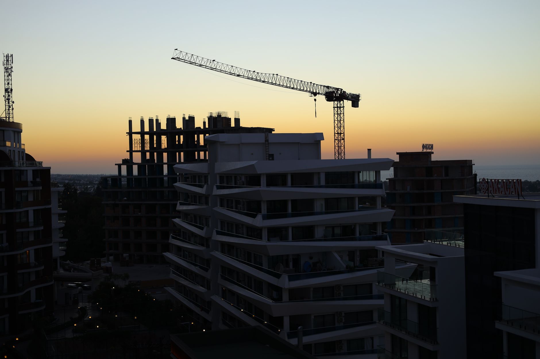 exterior of a half-constructed apartment building on the outskirts of Tehran at dusk, with a construction crane idle against a pale sky